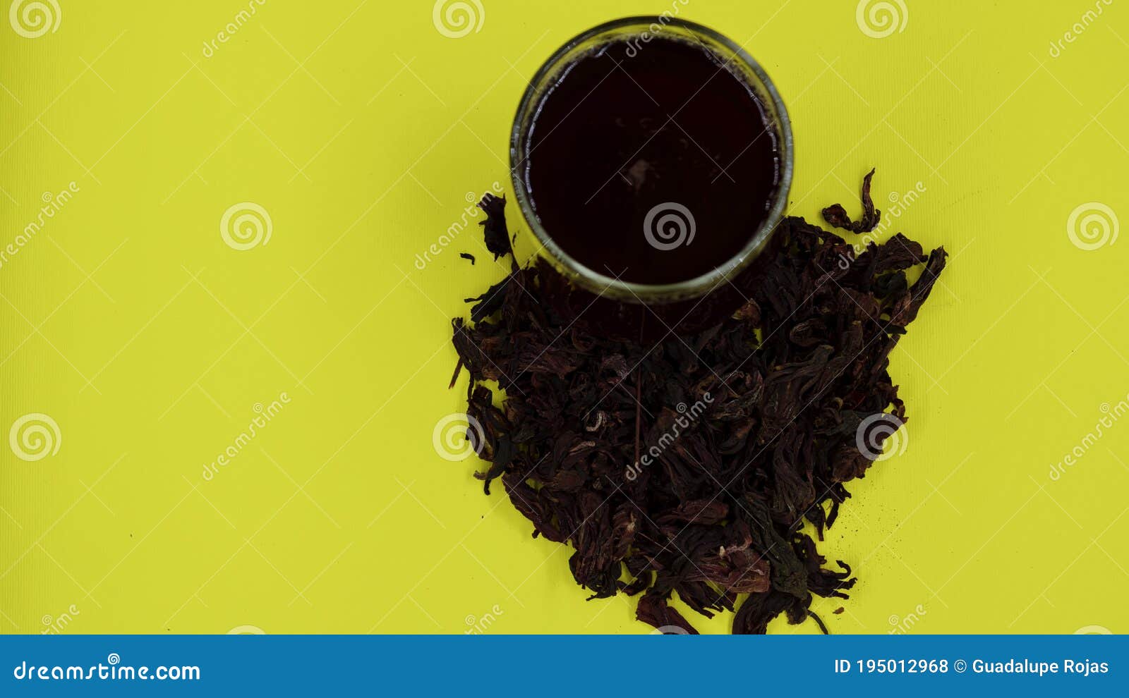glass cup with hibiscus water and hibiscus flower around on a yellow background