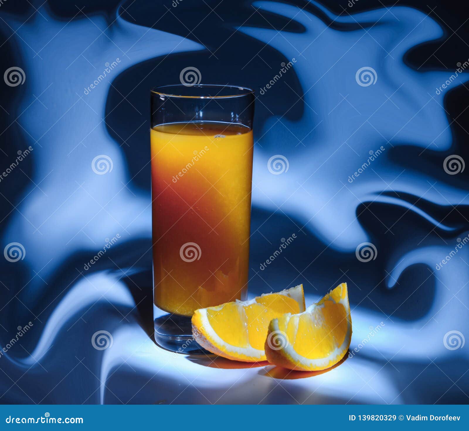 a glass of fresh orange juice and slices of orange on an abstracton blue background.