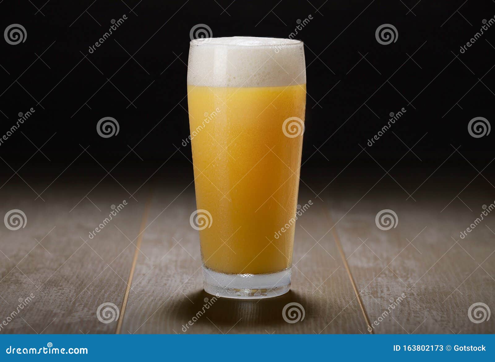 a glass of india pale ale, hazy unfiltered juicy draft beer on wooden surface and black background