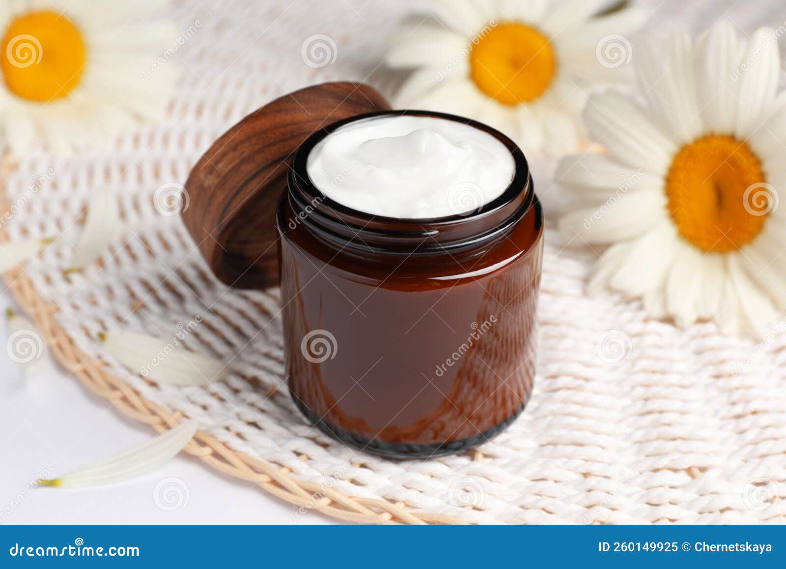 Glass Jar of Face Cream and Beautiful Flowers on White Table Stock
