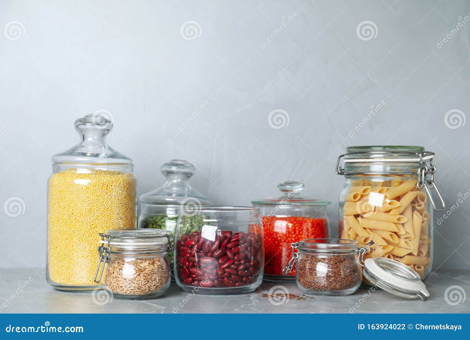 Glass Jars with Different Types of Groats on Grey Marble Table Stock