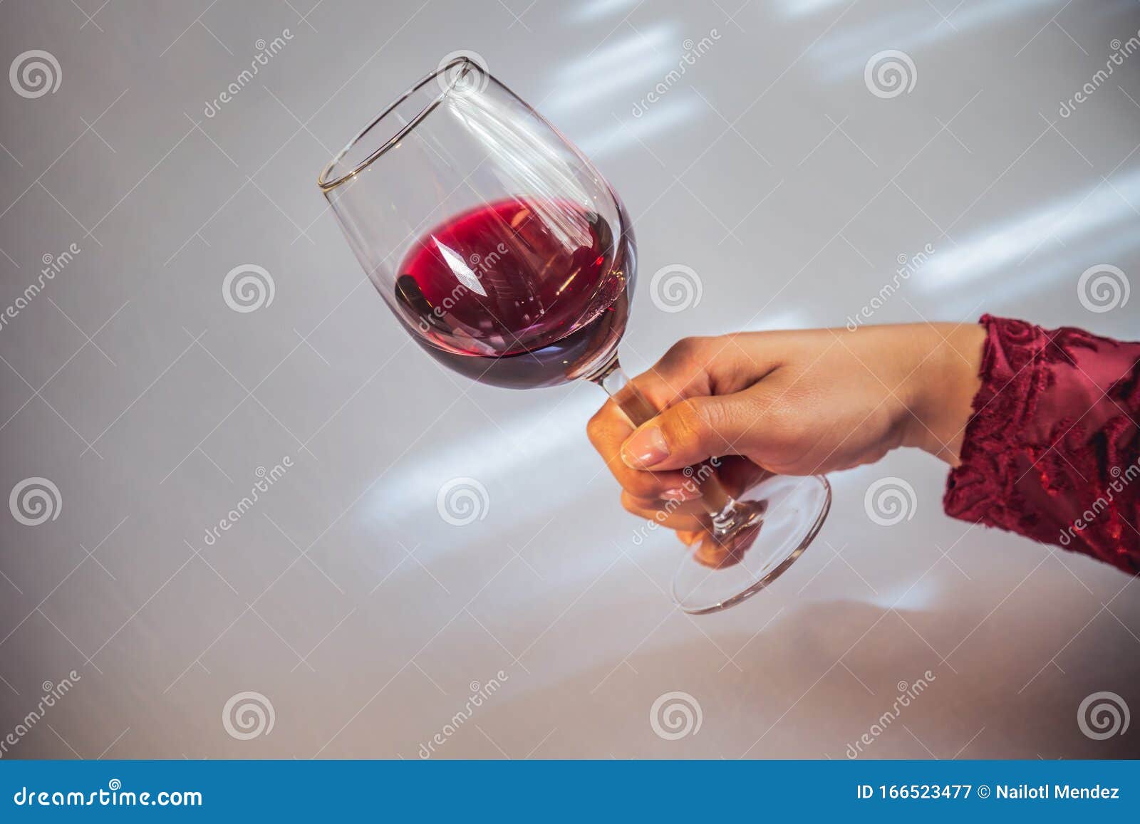 glass of red wine held by a woman& x27;s hand on white background