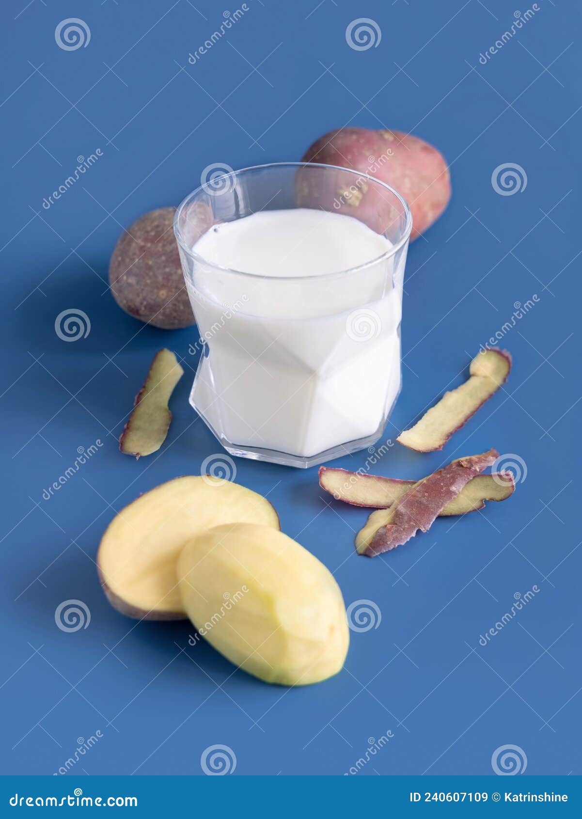 glass of vegetable potato milk on blue table near to potato tubers