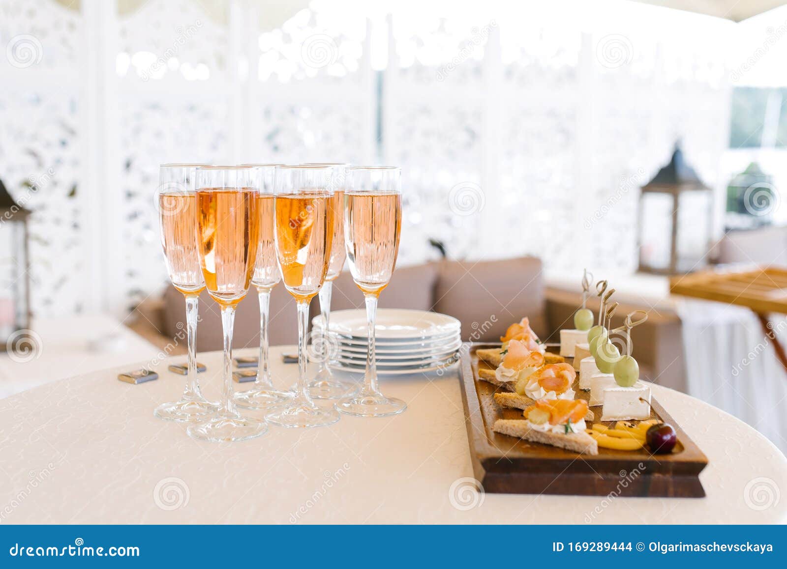 glasses of pink champagne stand on the buffet table next to a plate of appetizers