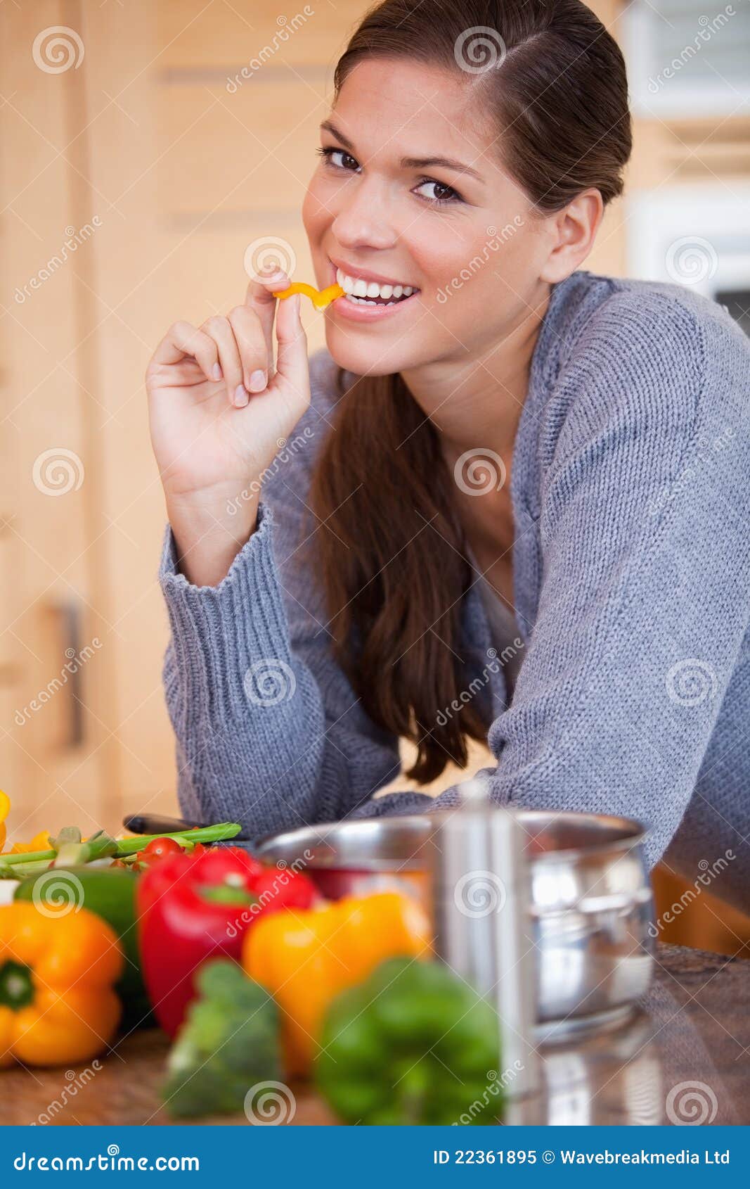 Glimlachende vrouw die een groene paprika in de keuken eet royalty ...