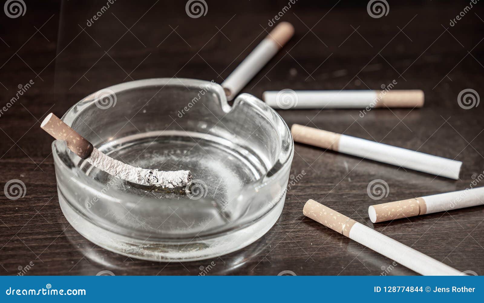 A Glimmering Cigarette Burns in an Ashtray on a Table Stock Photo