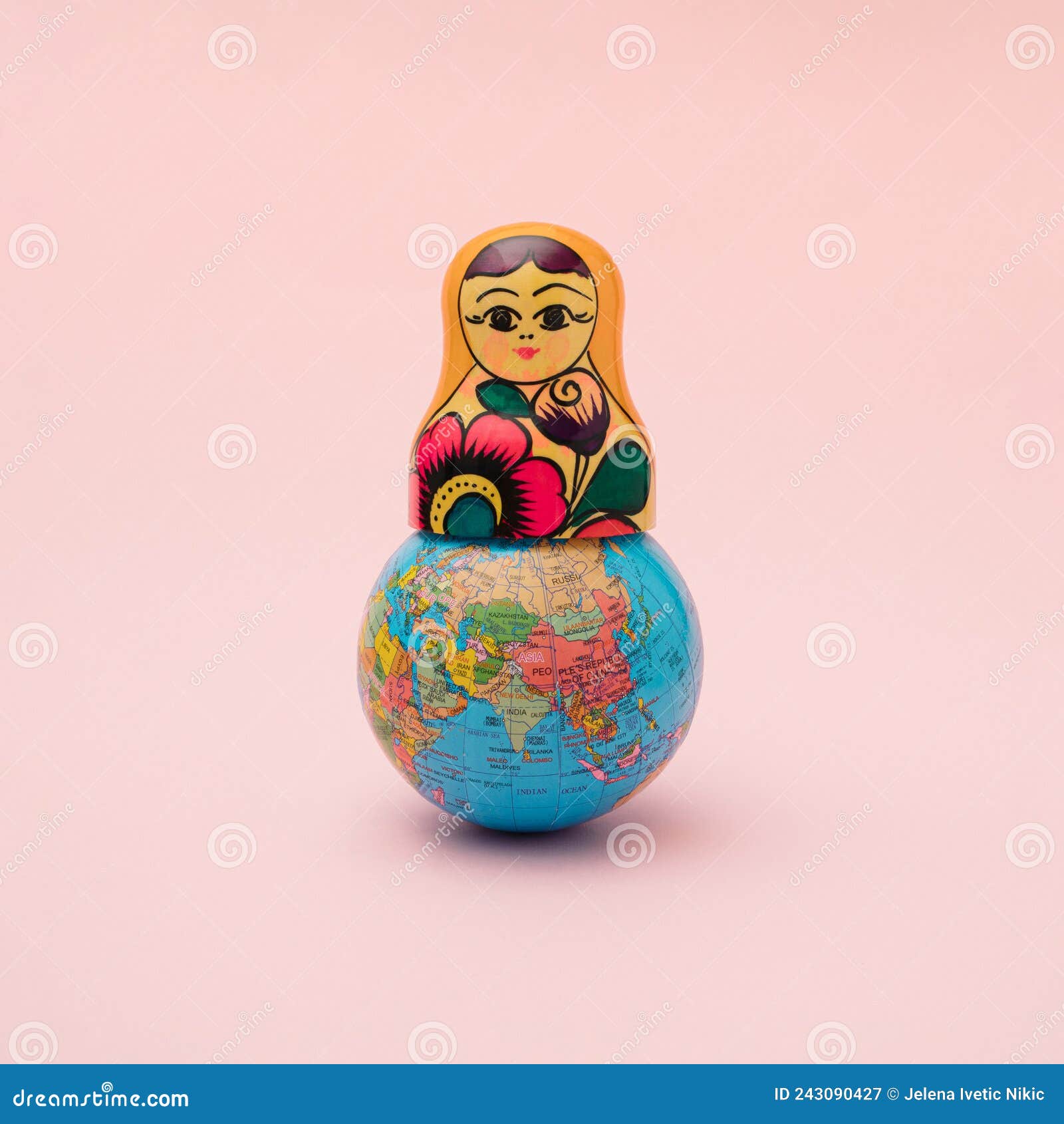 a globe with the upper part of a russian traditional wooden doll. minimal concept of events on the planet. pastel pink background