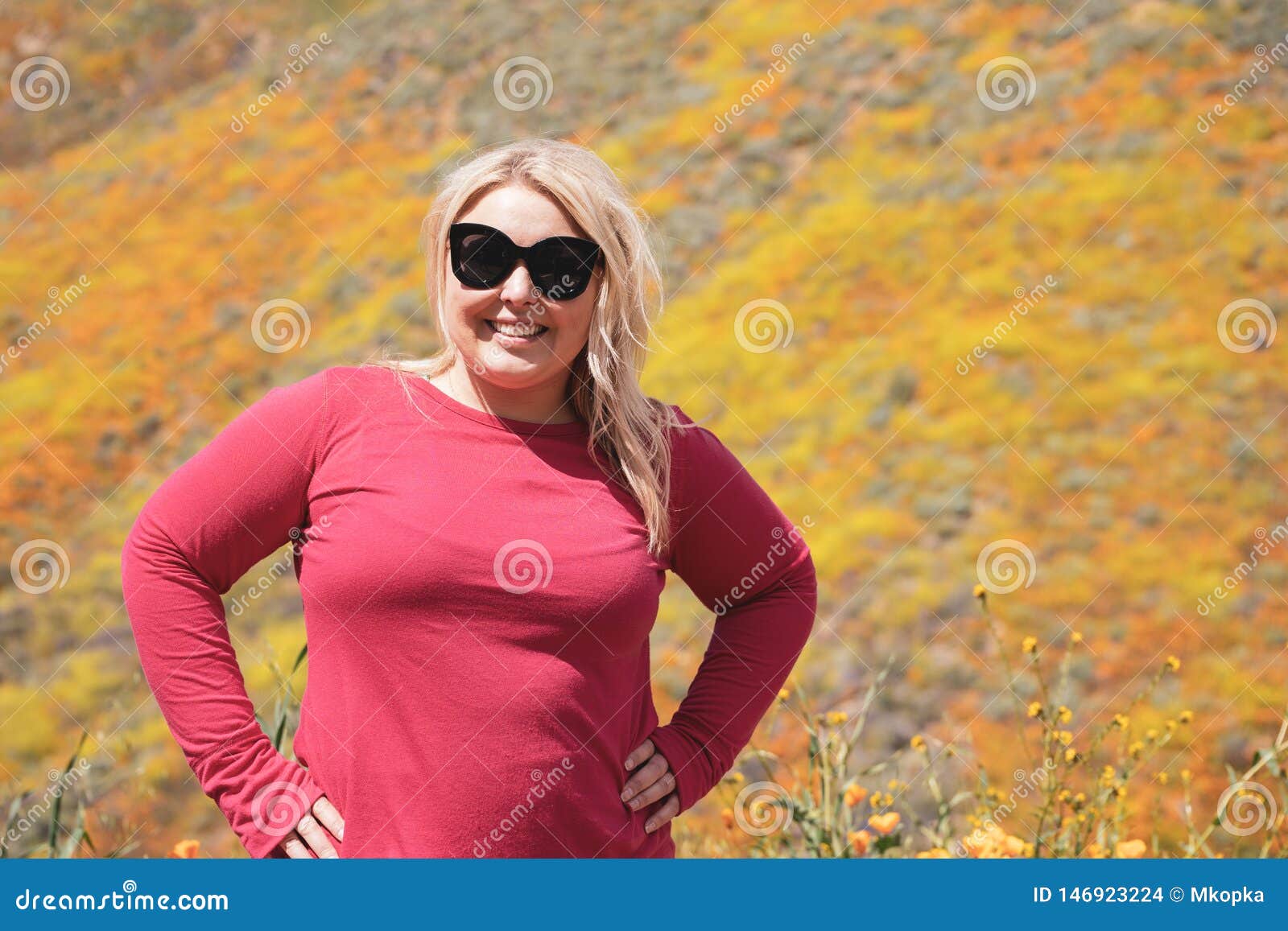 Glückliche erwachsene Frau, die mit Sonnenbrille während der Kalifornien-Superblüte von Mohnblumen bei Walker Canyon aufwirft