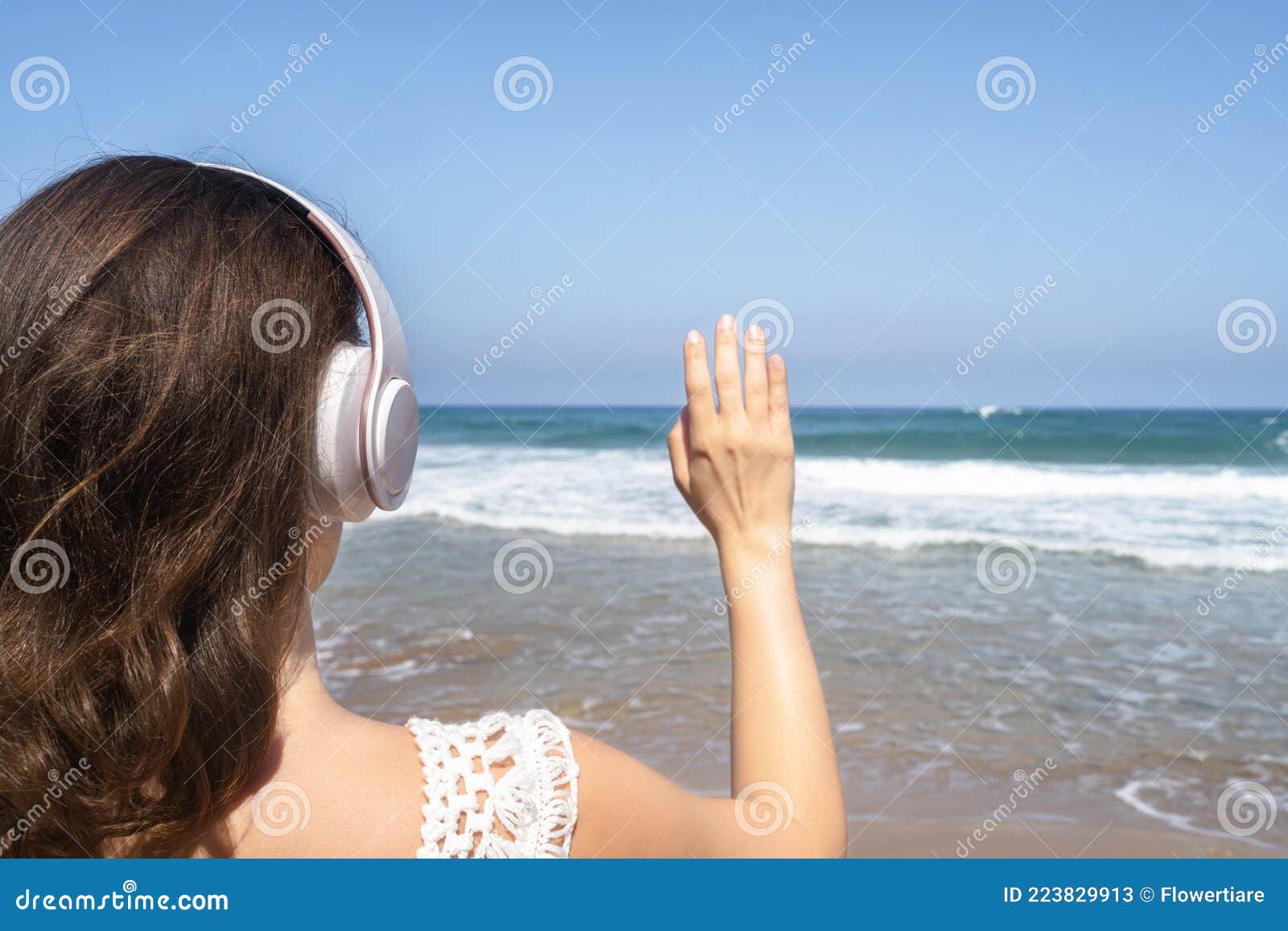 Glückliche Frau in Kopfhörern Hören Musik Winkende Hand Zu Sagen Hallo Und  Einladende Meer am Strand Stehen. Sommerferien. Rücksei Stockbild - Bild  von stehen, hand: 223829913