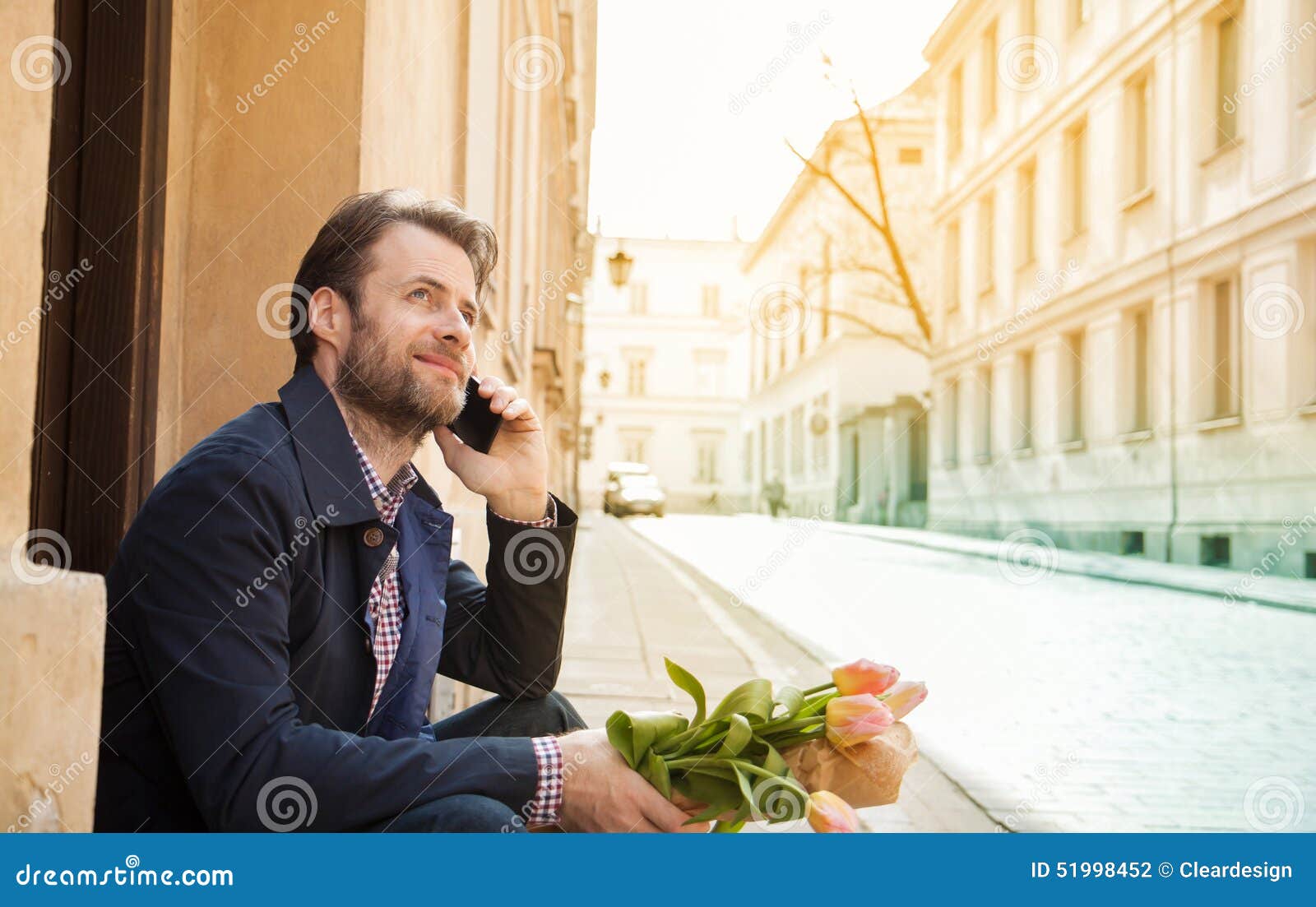 Glücklicher lächelnder Mann mit Blumenblumenstrauß sprechend an einem Handy - Stadt. Glückliches lächeln vierzig Jahre alte kaukasische Mann mit Blumenblumenstrauß sprechend an einem Handy Straßen- und Stadtgebäude als Hintergrund