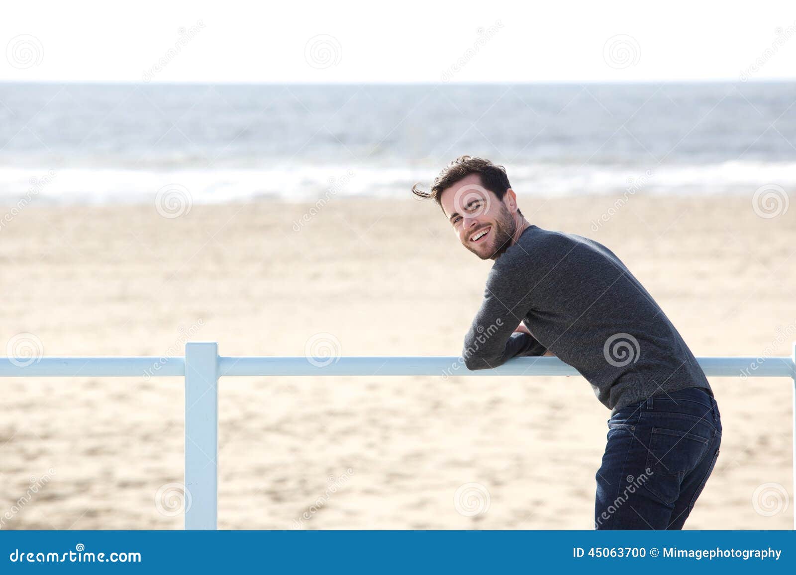 Glücklicher Mann, der allein am Strand steht. Porträt eines glücklichen jungen Mannes, der allein am Strand steht