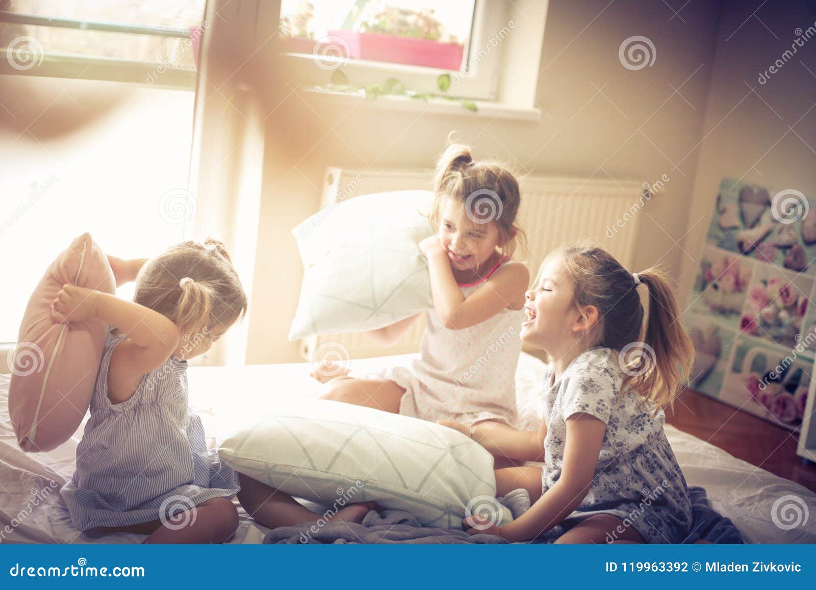 Glücklicher Morgen Kinder im Bett. Drei kleine Mädchen, die im Bett spielen und Kampf mit Kissen haben Raum für Kopie