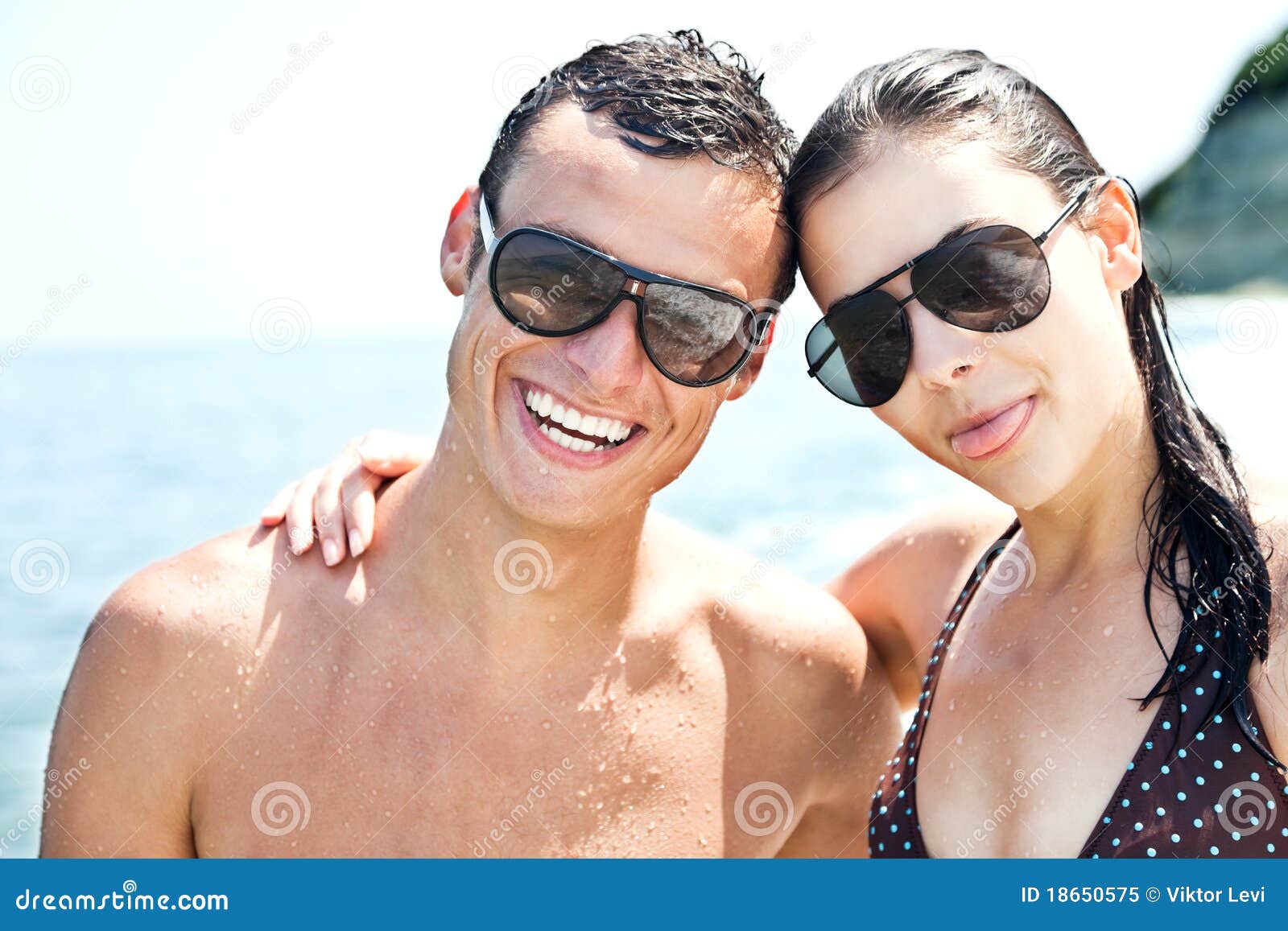 Glücklicher Paarstrand. Glückliche Paare mit den Sonnenbrillen, die auf Strand, Frau mit der Zunge heraus umarmen und lächeln