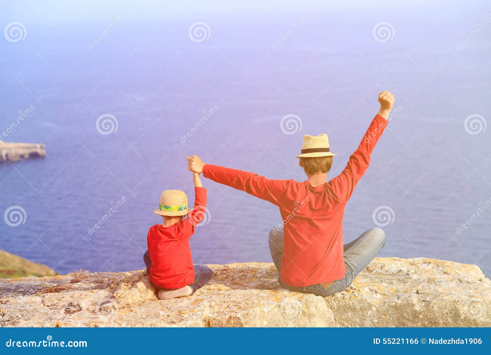 Glücklicher Vater und Sohn, die auf einen Berg sitzt. Der Vater und Sohn, die auf einen Berg ausdrückt Freude mit ihren Armen sitzt, dehnten oben in Richtung zum Himmel aus