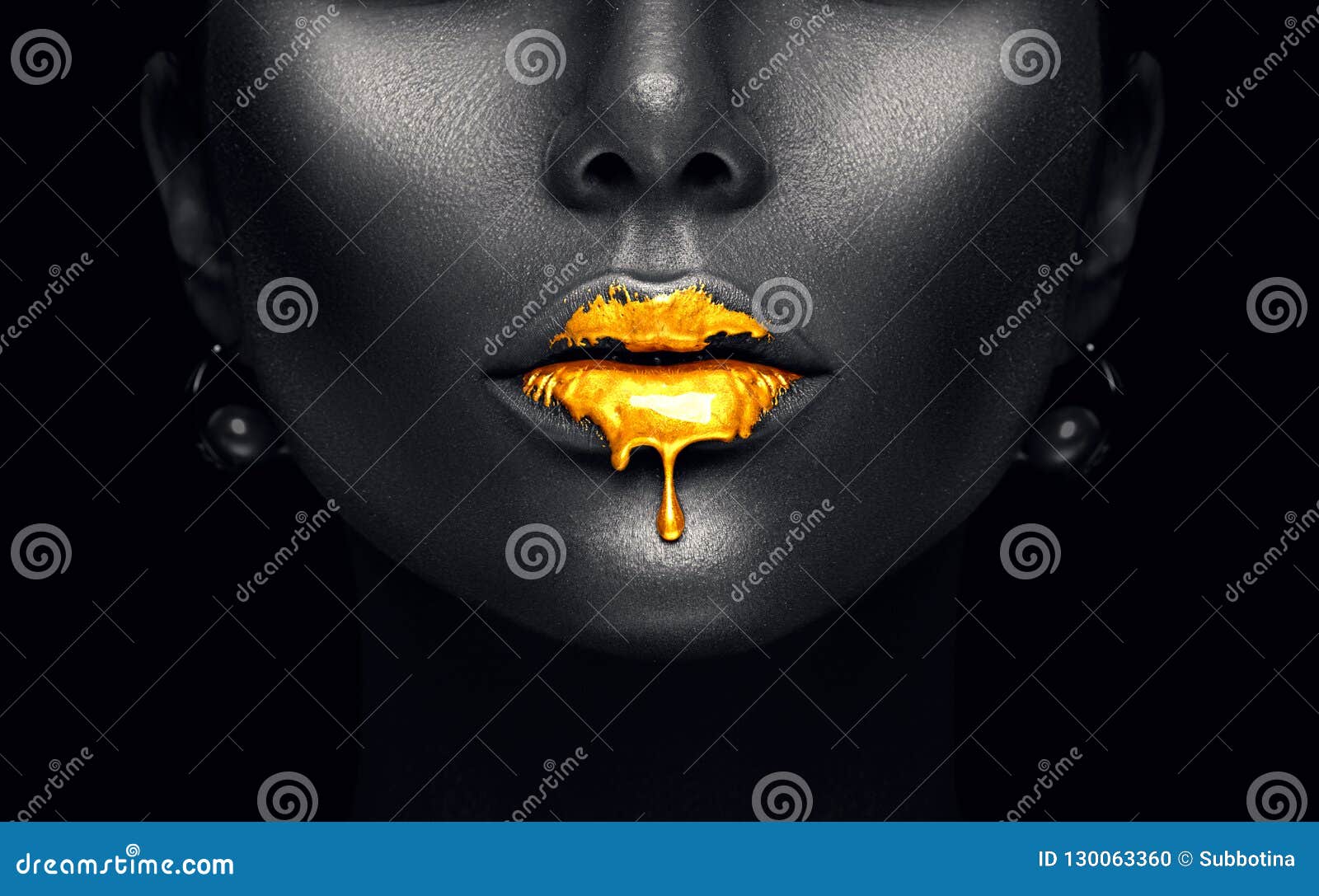 gold paint drips from the lips, golden liquid drops on beautiful model girl`s mouth, creative abstract dark black skin makeup