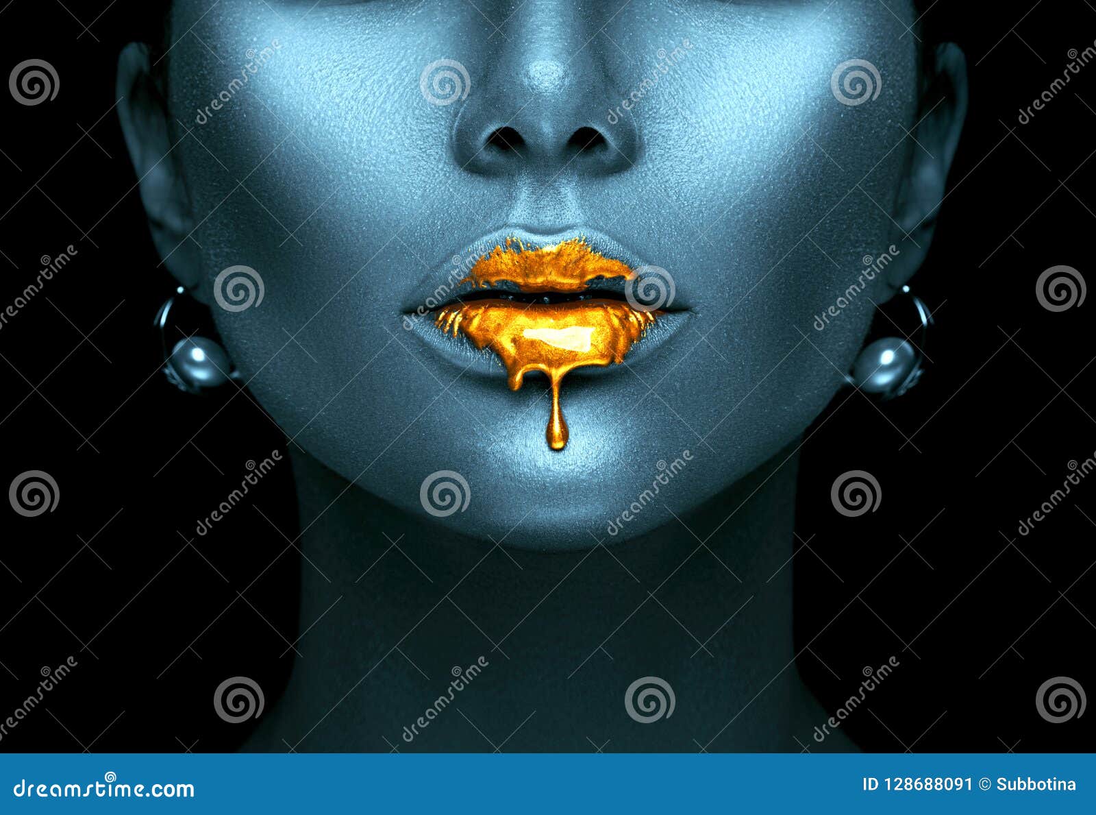 gold paint drips from the lips, golden liquid drops on beautiful model girl`s mouth, creative abstract dark blue skin makeup