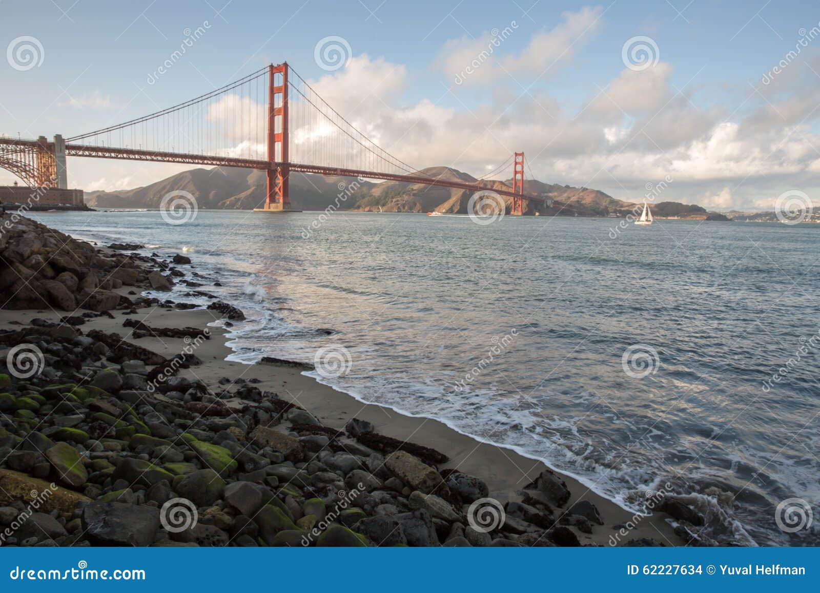 Golden gate bridge da punto forte a San Francisco. Contenuto un pomeriggio nuvoloso piacevole, con una barca a vela e un fondo muscoso delle rocce