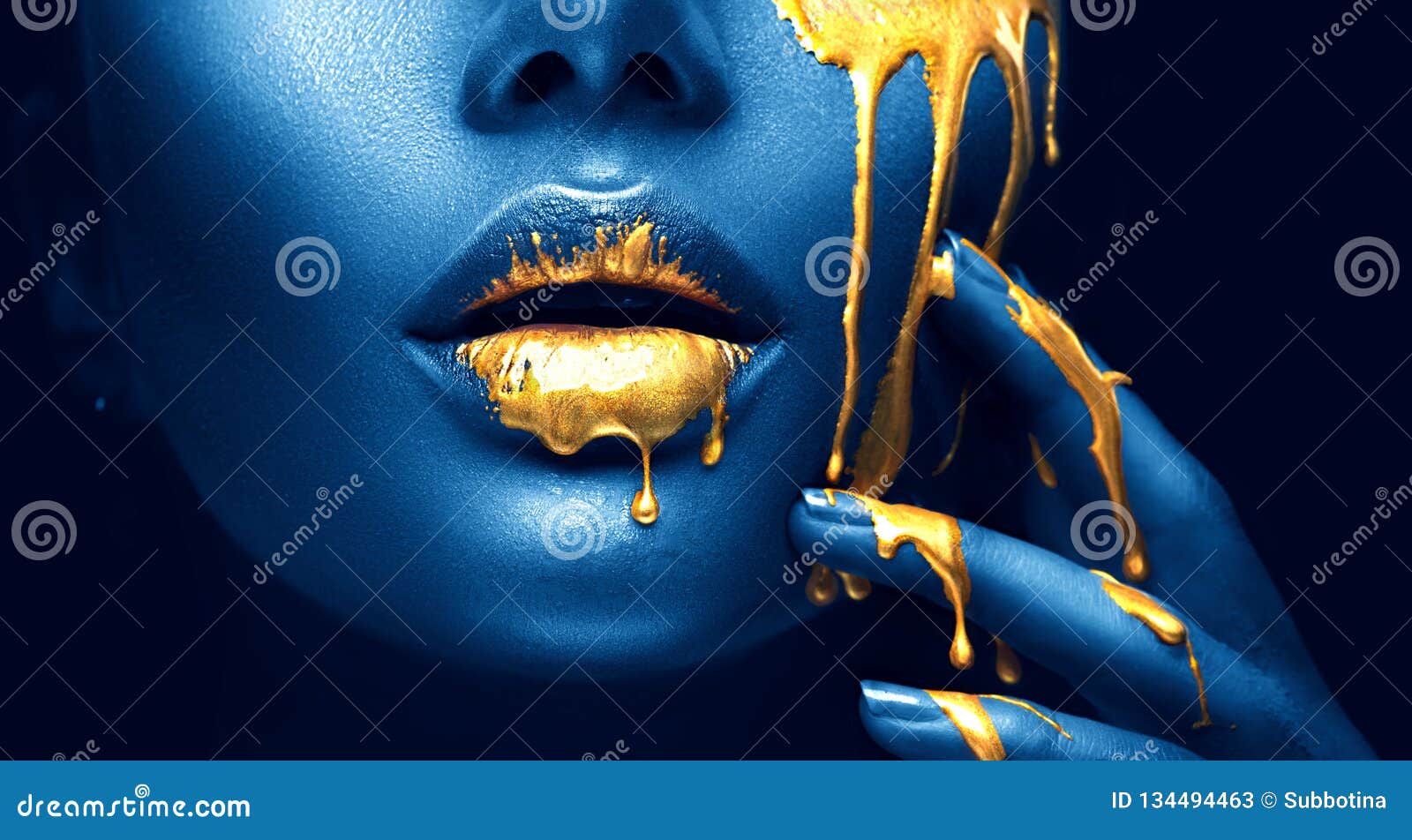 golden paint smudges drips from the face lips and hand, golden liquid drops on beautiful model girl`s mouth, creative makeup