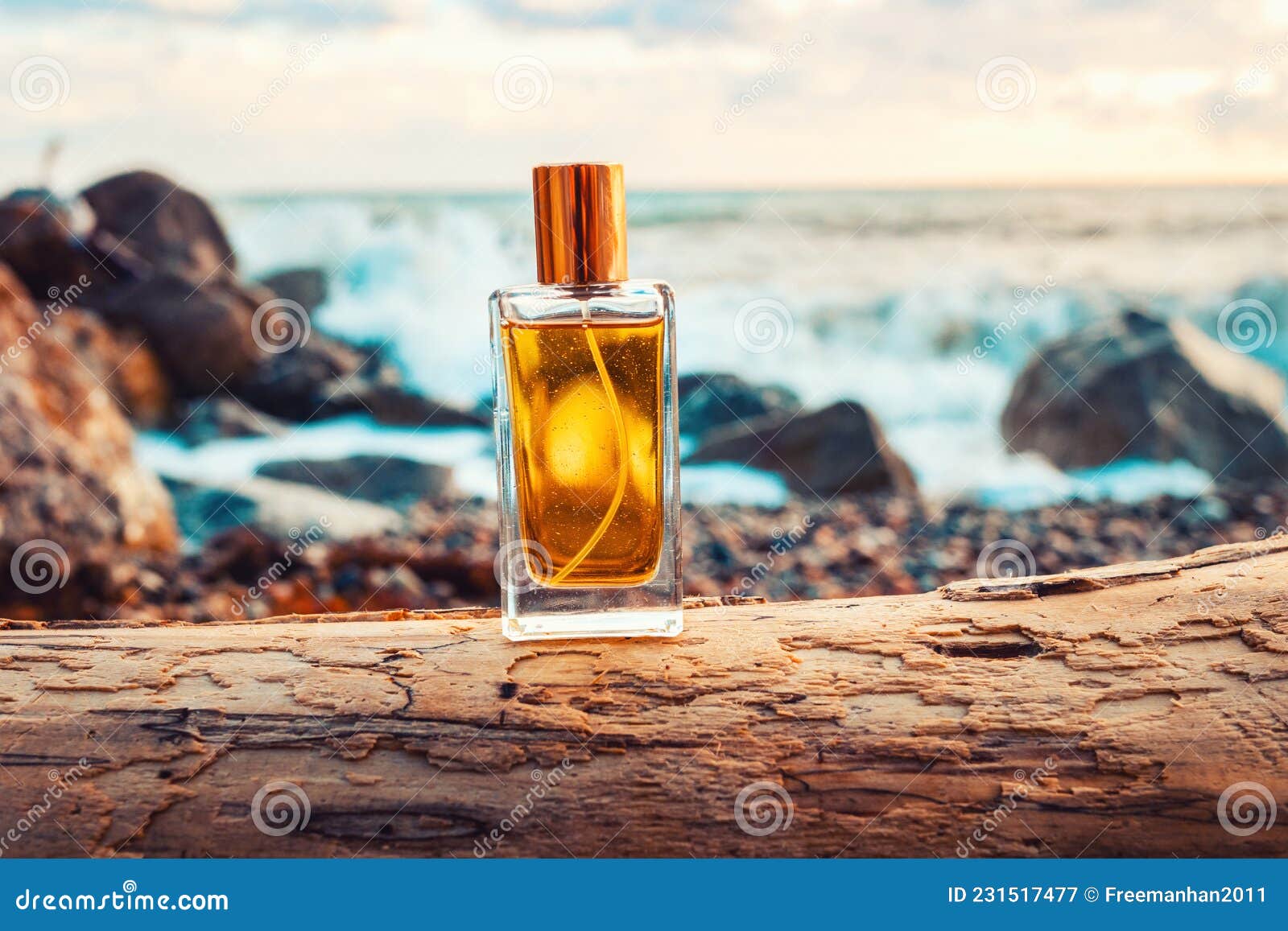 A golden transparent perfume bottle with drops on a wet pebble beach.  Close-up. In the background, the sea surf is blurred. Perfume advertising  concept Stock Photo