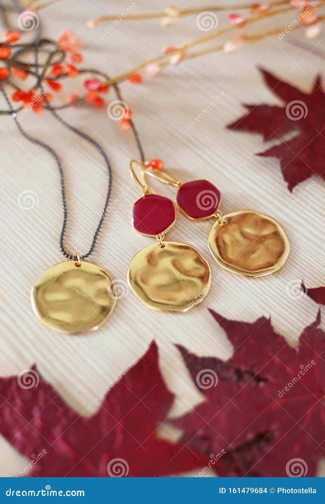 Goldene Ohrringe mit roten Steinen und Halsketten - rote Blätter auf HolzHintergrund. Stillleben der goldenen Ohrringe mit roten Steinen und Halsketten - rote Blätter auf Holzboden