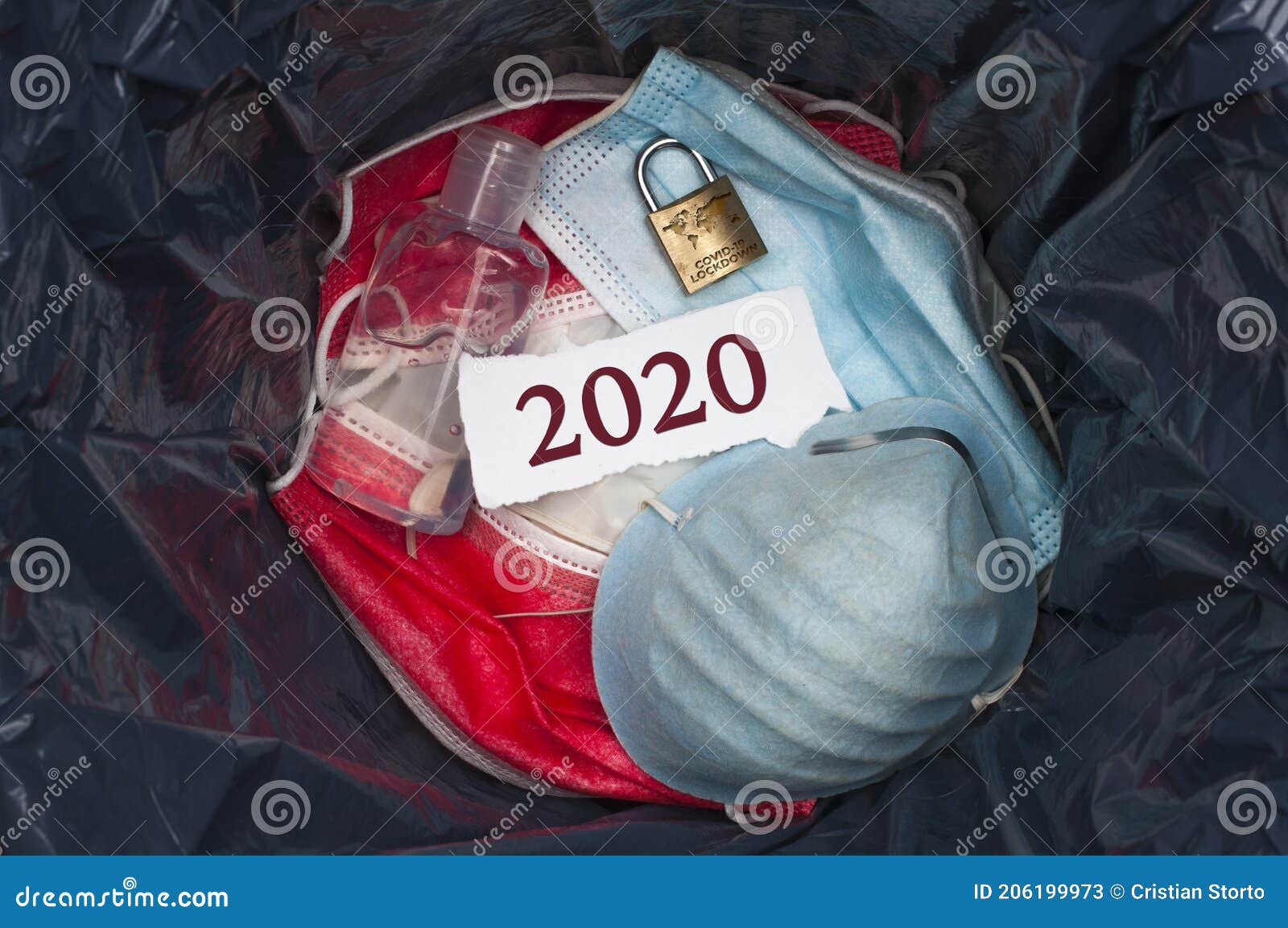 goodbye 2020 concept: the inside of a trashbin with surgical masks, sanitizing gel, a padlock and a slip of paper with the