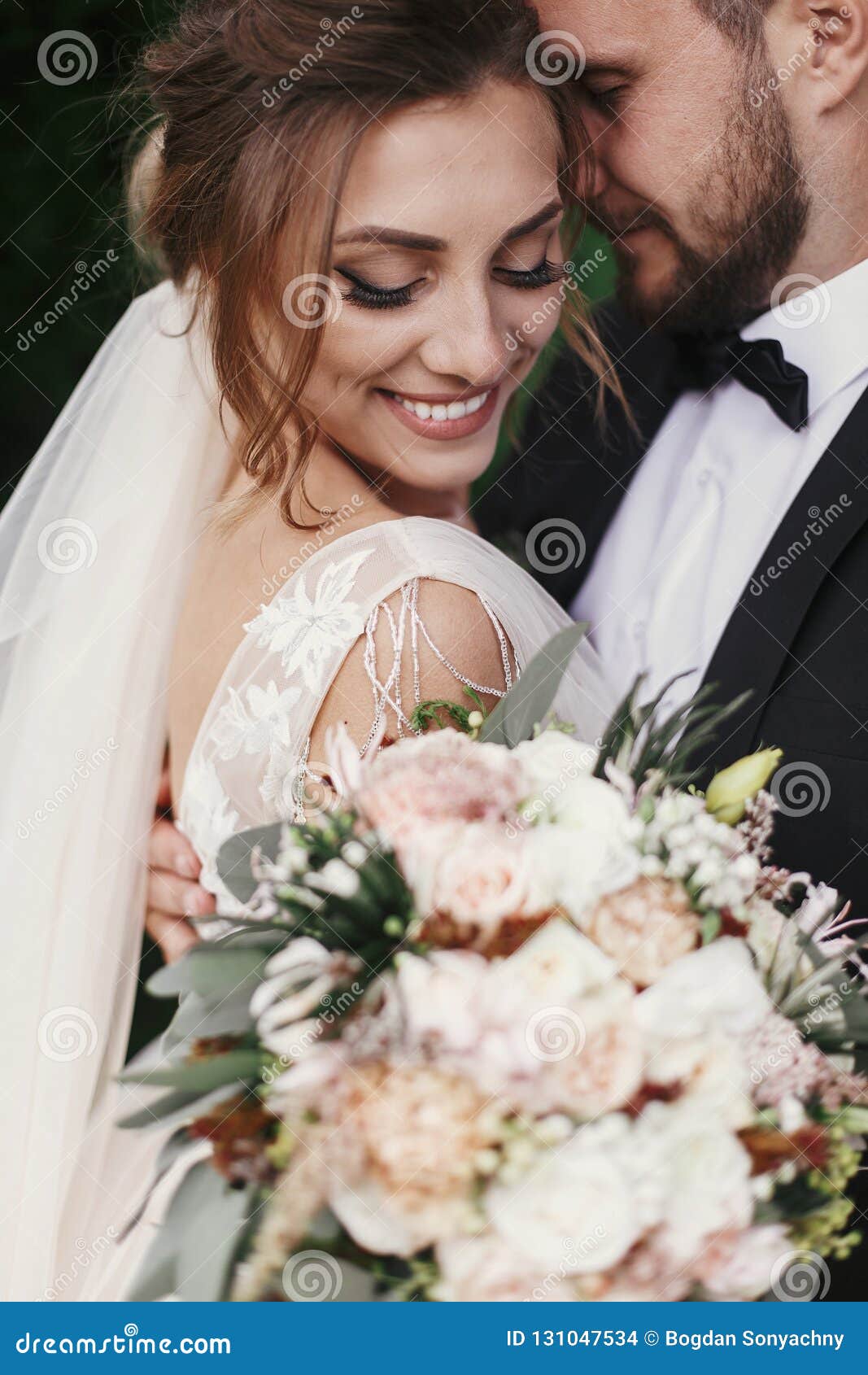 gorgeous bride and stylish groom gently hugging and smiling on b