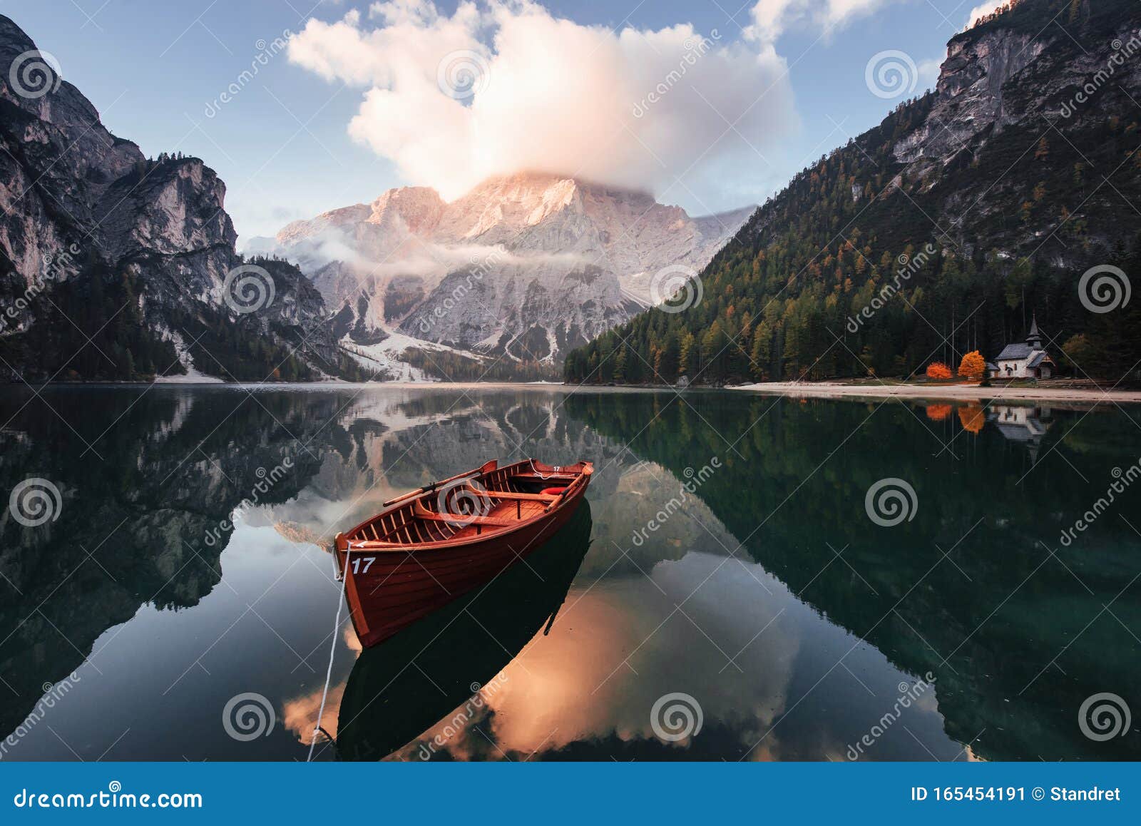 gorgeous landscape. wooden boat on the crystal lake with majestic mountain behind. reflection in the water. chapel is on