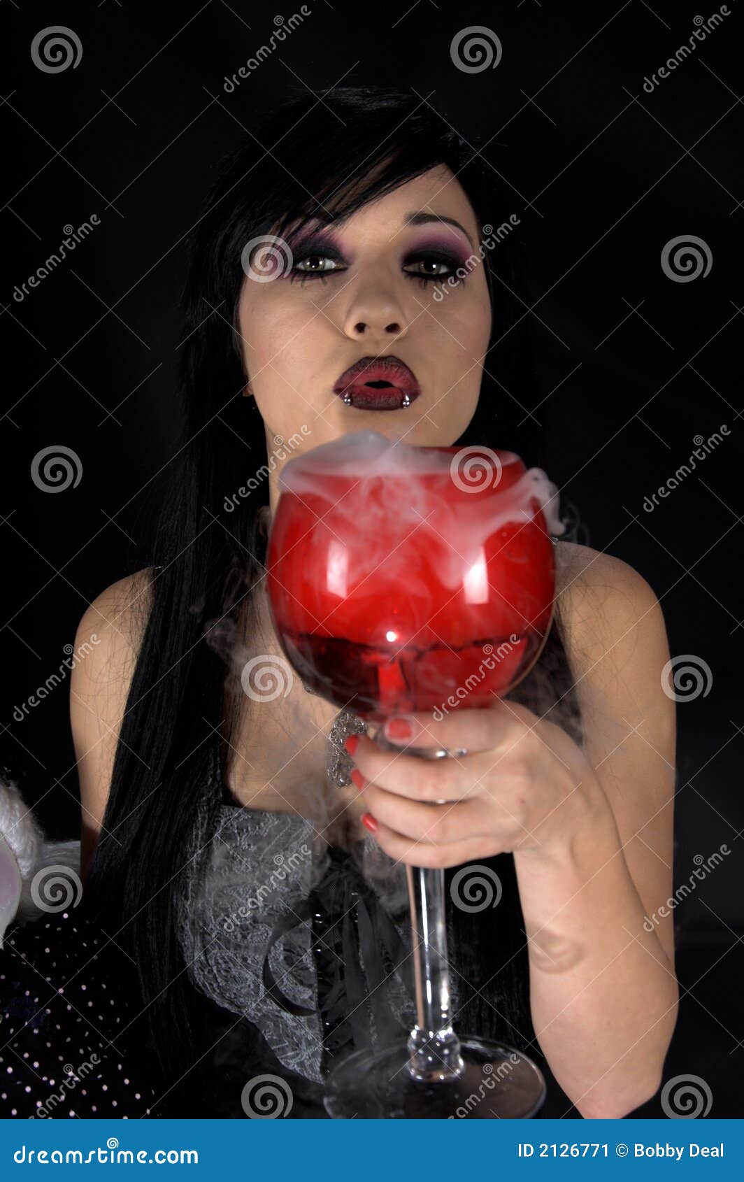 Gothic Woman Witches Brew. Beautiful raven haired gothic Vampire girl in a black and grey dress blowing on a steaming goblet of Witches Brew