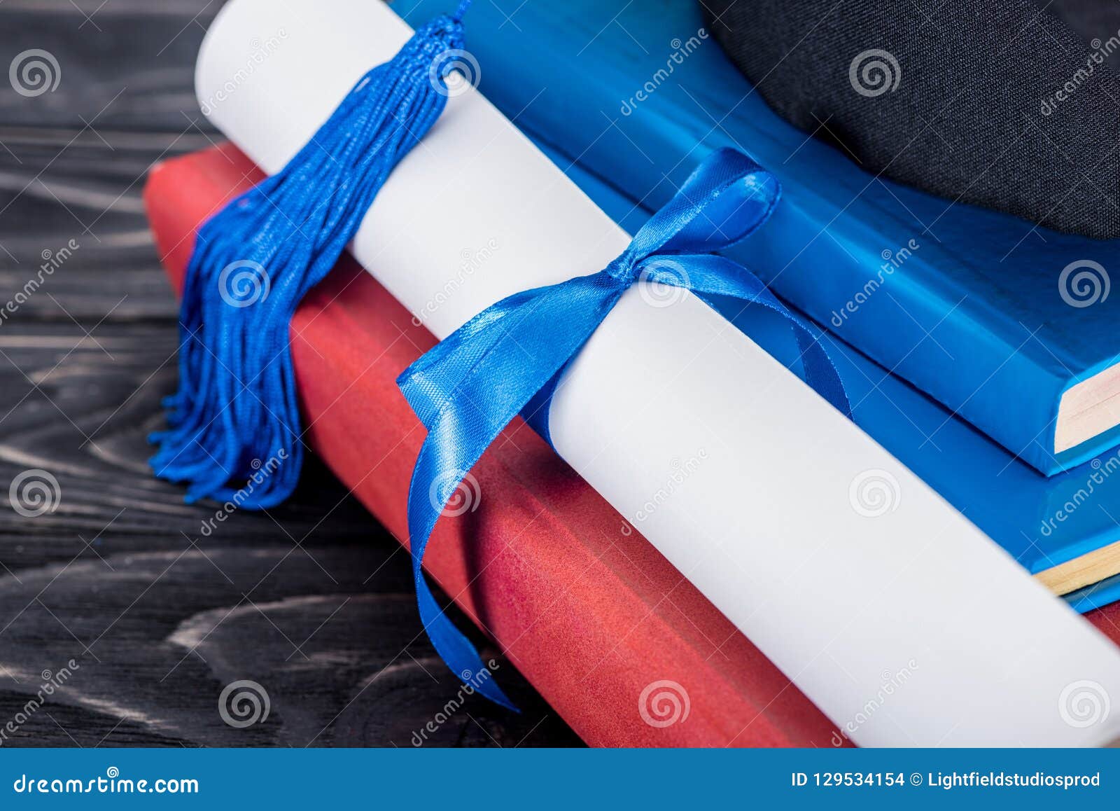 Graduation Hat and Diploma with Blue Ribbon on Stack Stock Photo