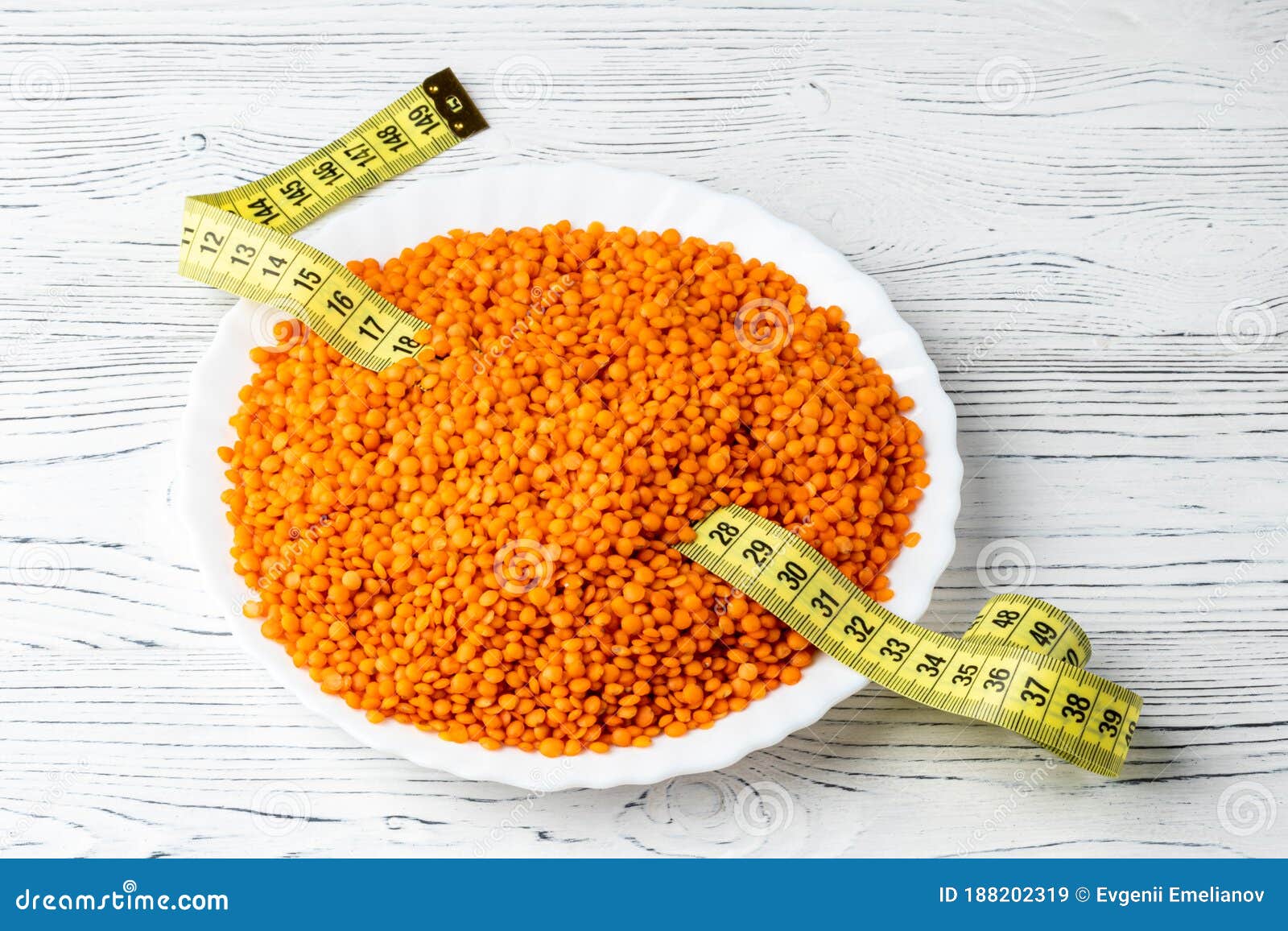 grains of red lentils and a measuring tape in a plate on a white wooden table