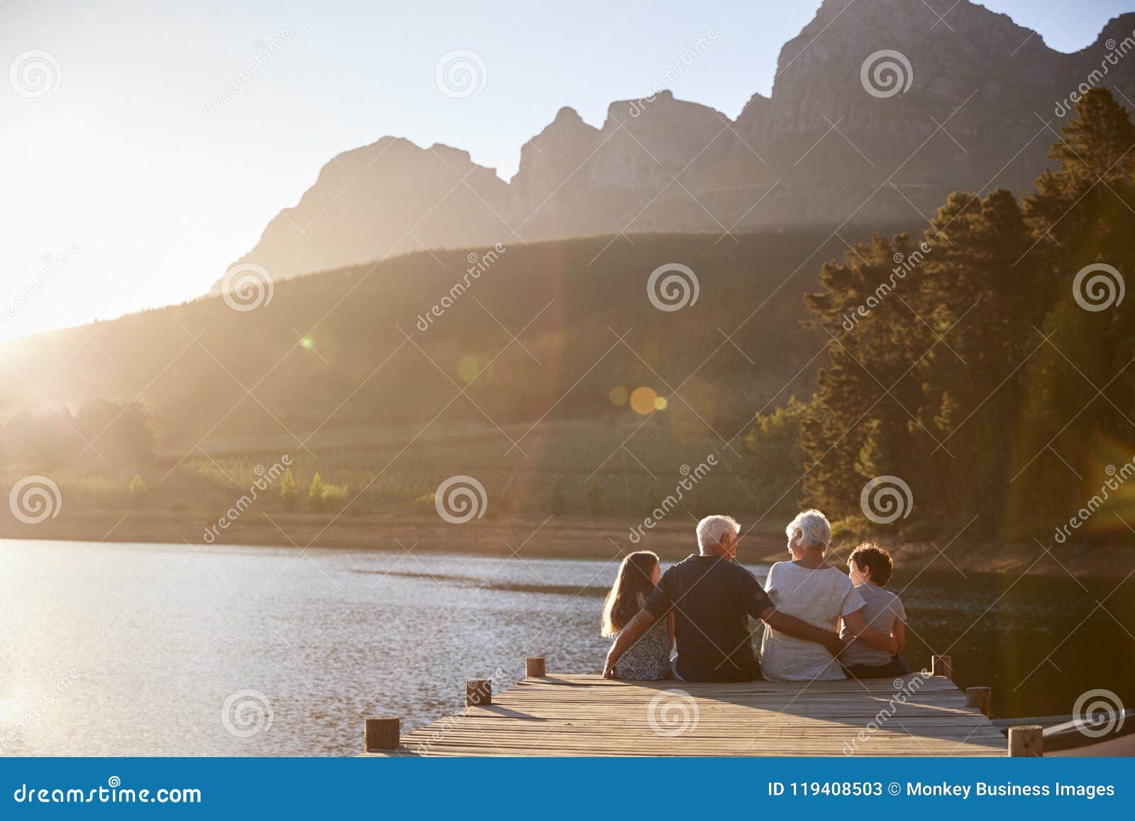 grandchildren with grandparents sitting on wooden jetty by lake