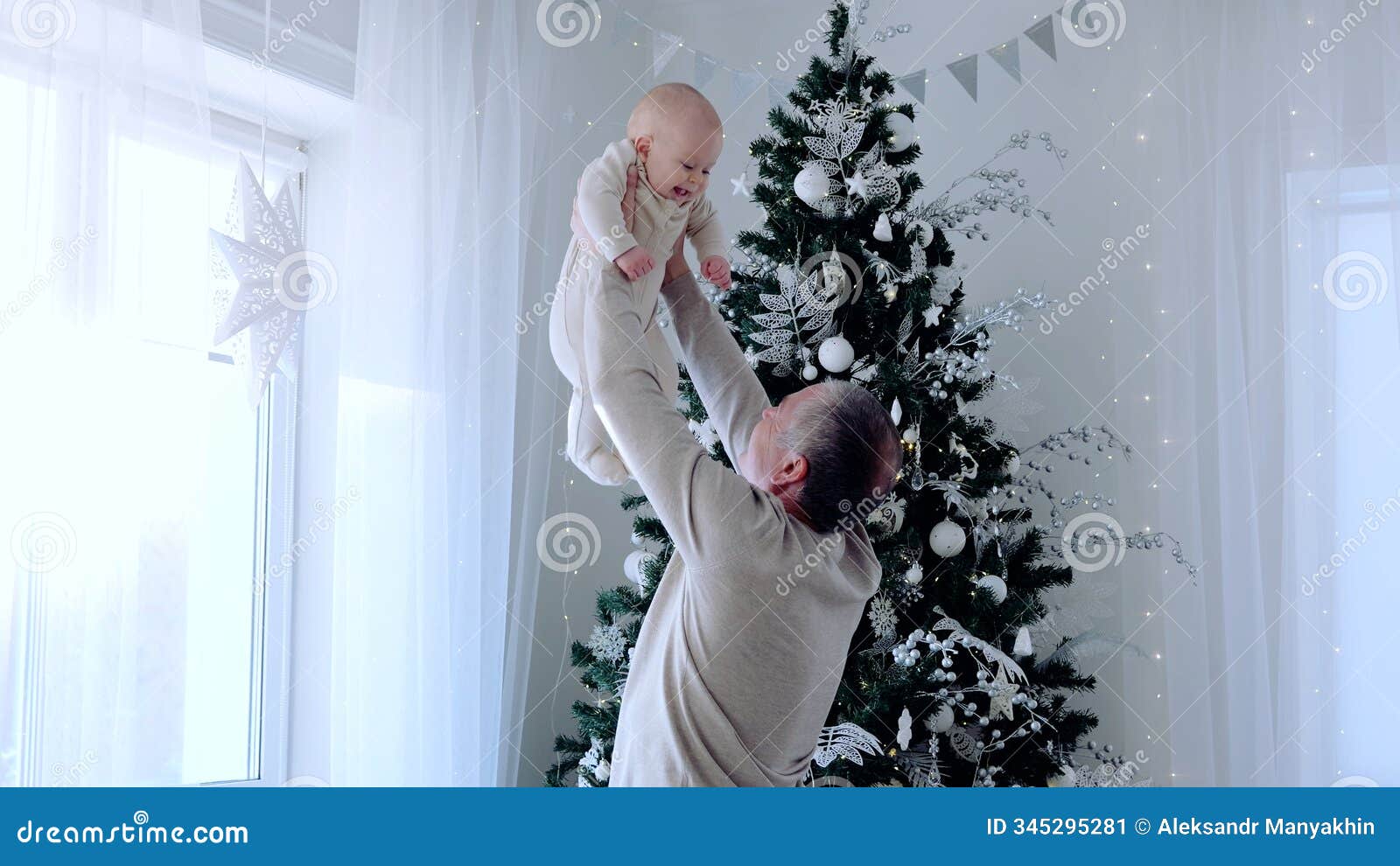 grandfather lifting baby granddaughter near a festive christmas tree in a holiday decorated room with star d lights