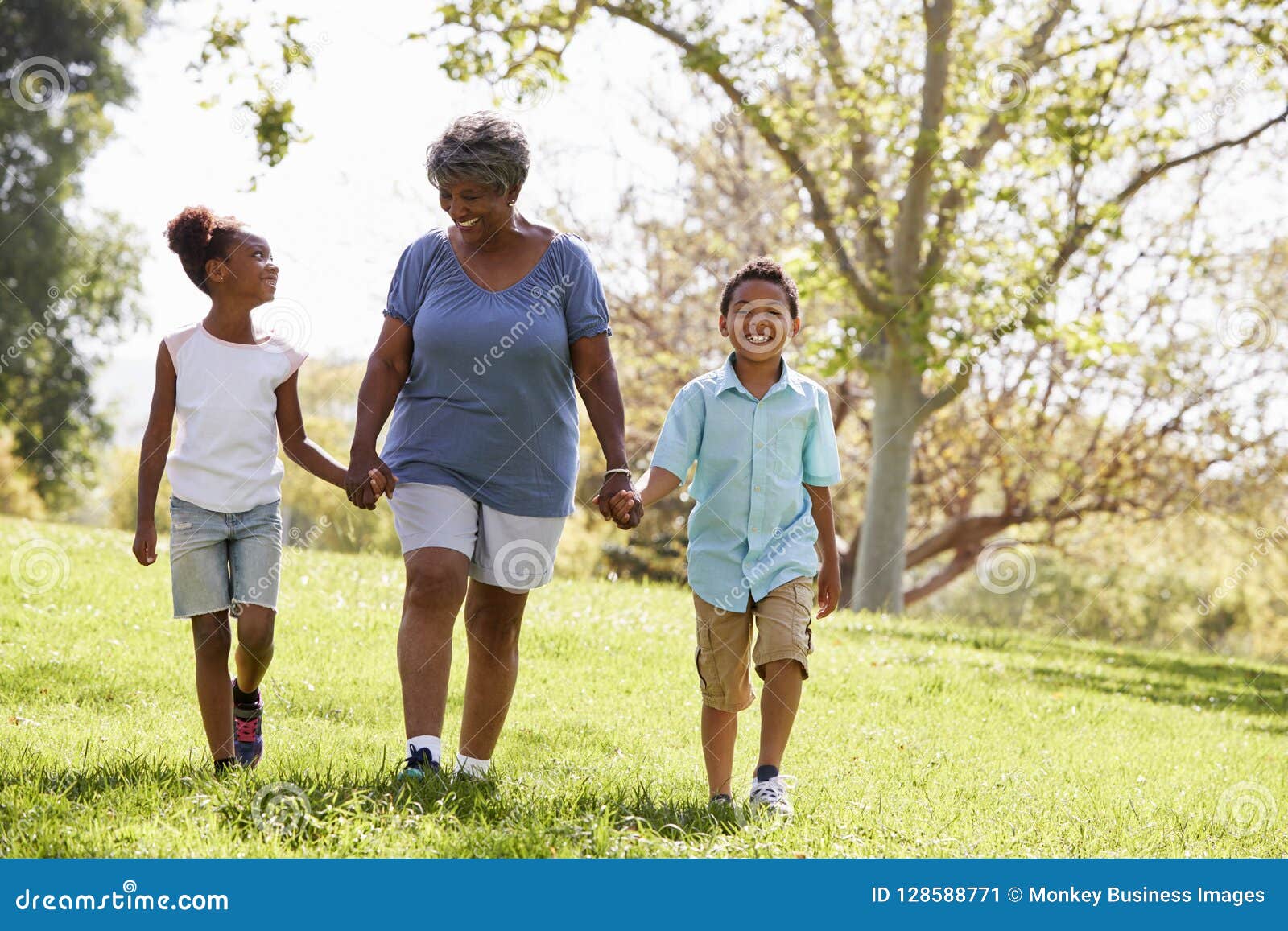 grandmother walking in park and holding hands with grandchildren