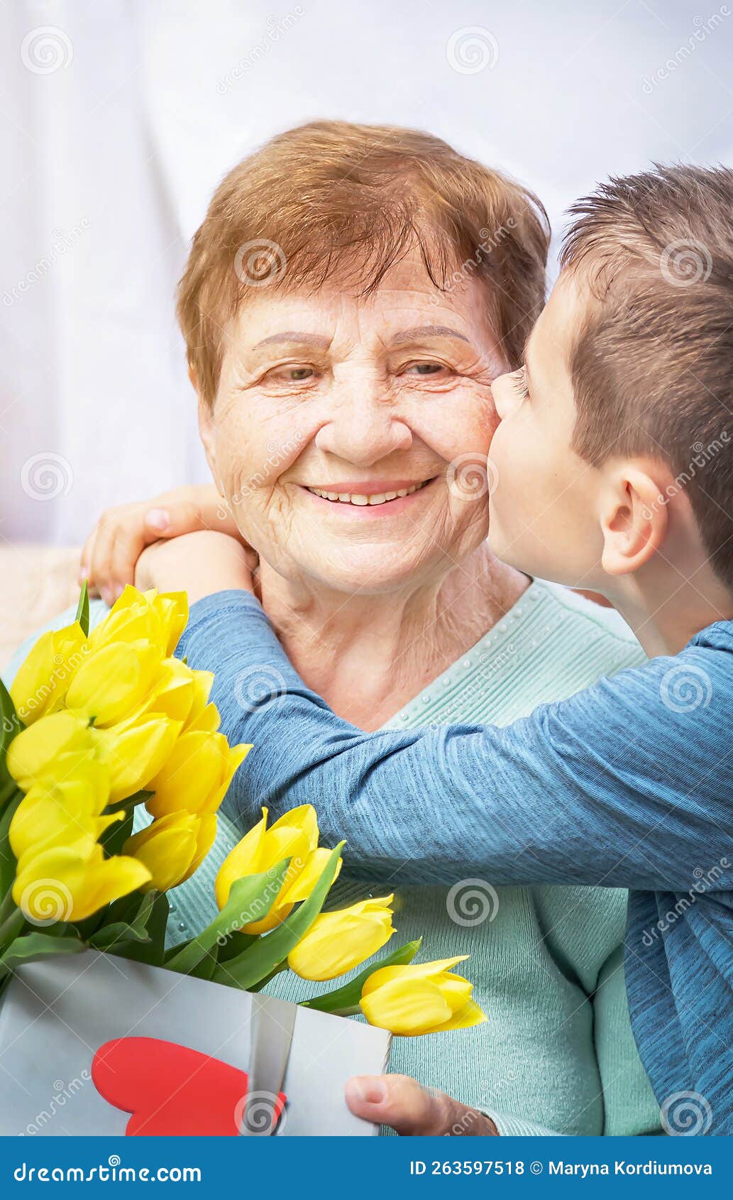 grandson congratulates grandma on holiday. grandmother has bunch of yellow flowers tulipan.