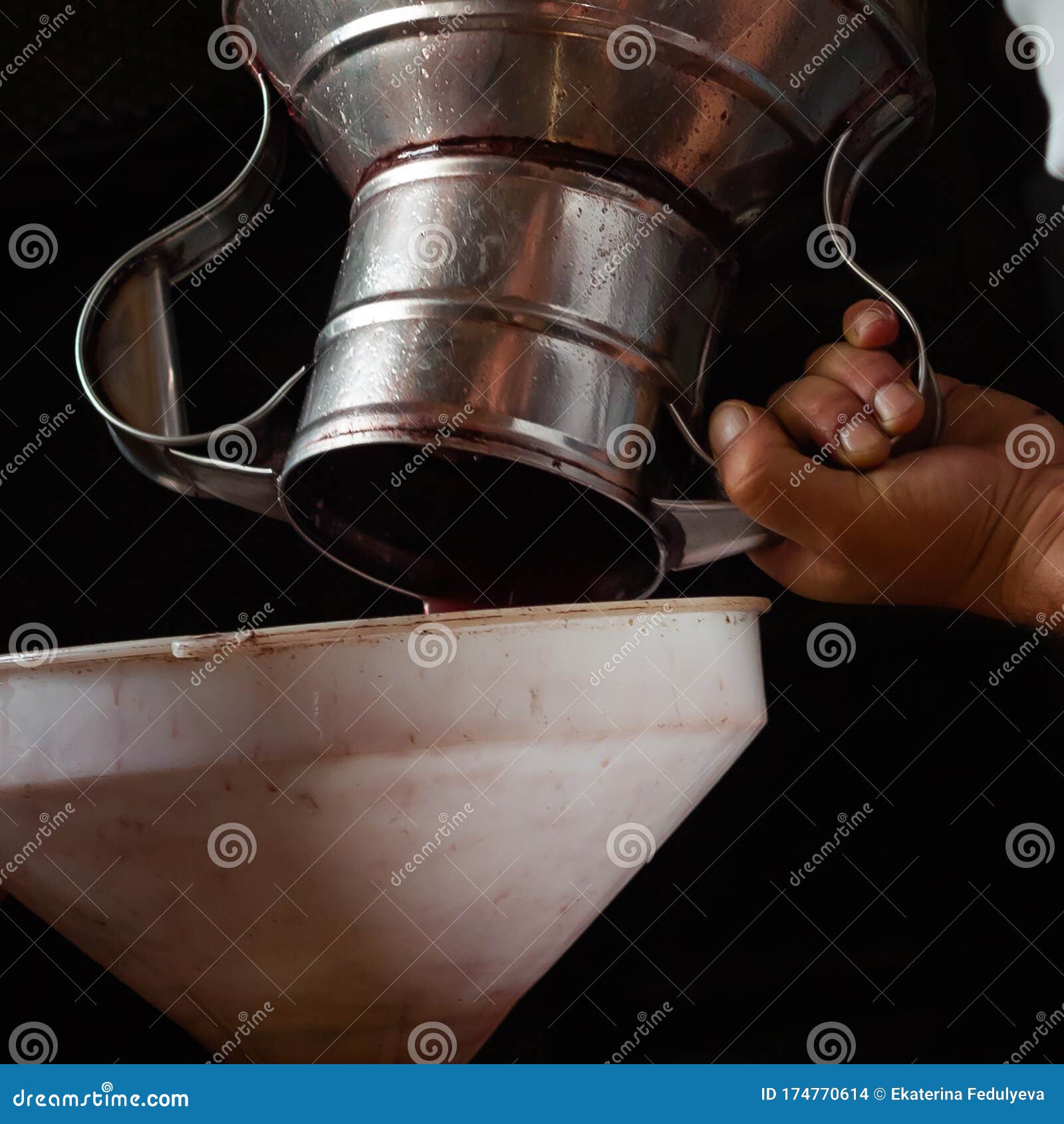 grape harvest, a man`s hands pour grape jiuce from a steel jug into a white funnel