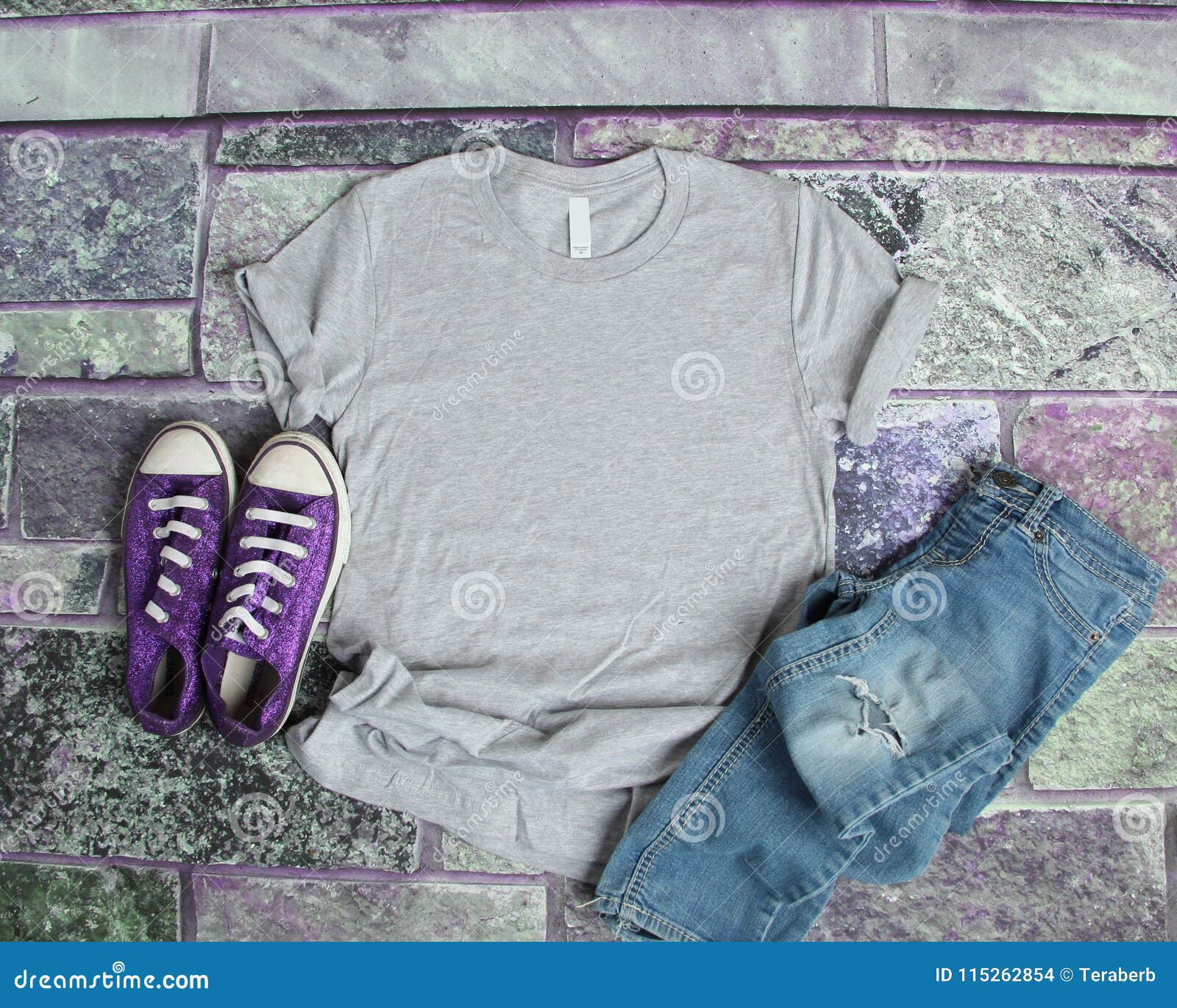 gray t shirt mockup flat lay on purple brick background with purple shoes and ripped jeans