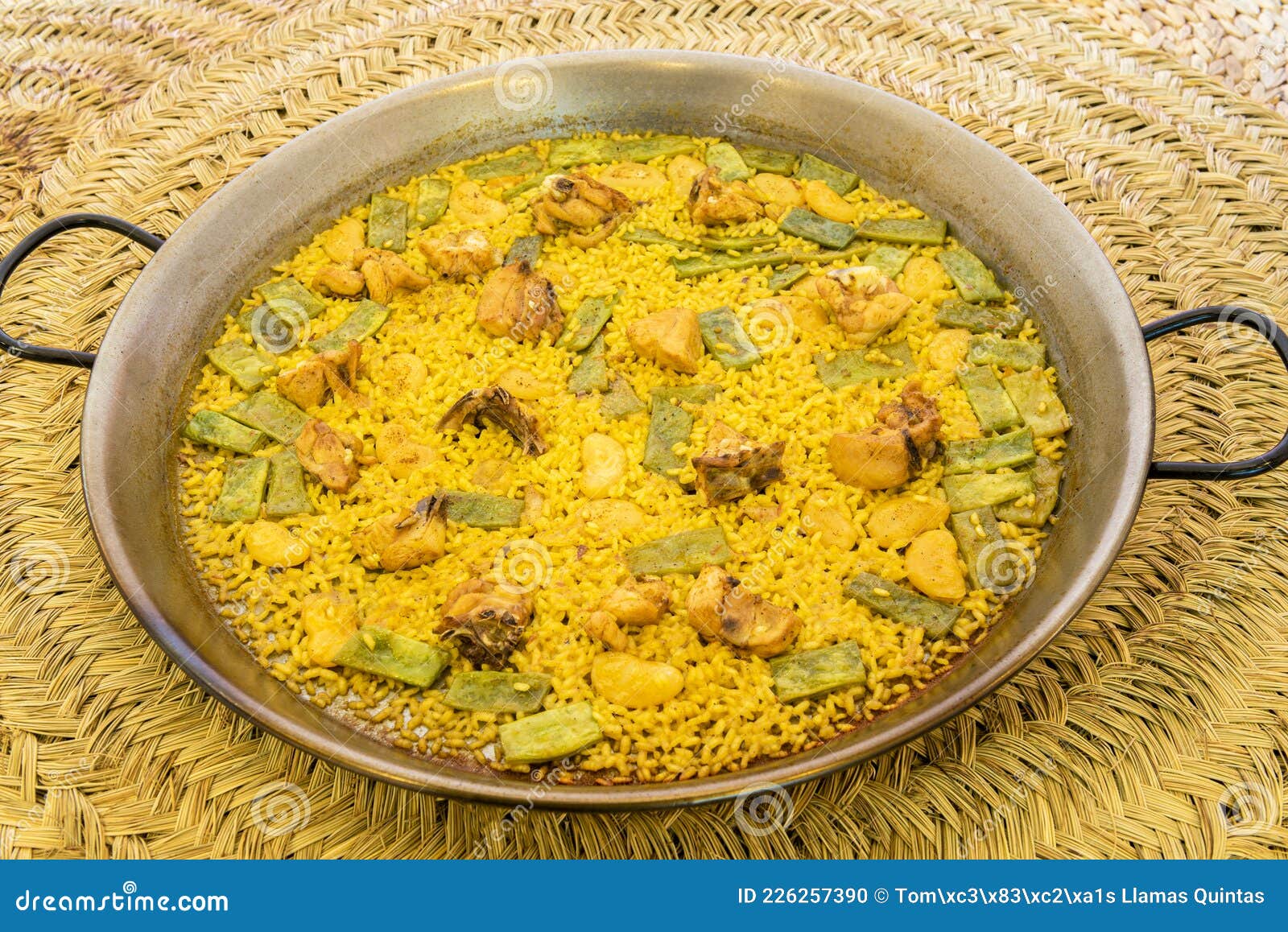 great and popular valencian rice paella presented in a paella pan with green flat beans, chunks of stewed chicken, white garrafon
