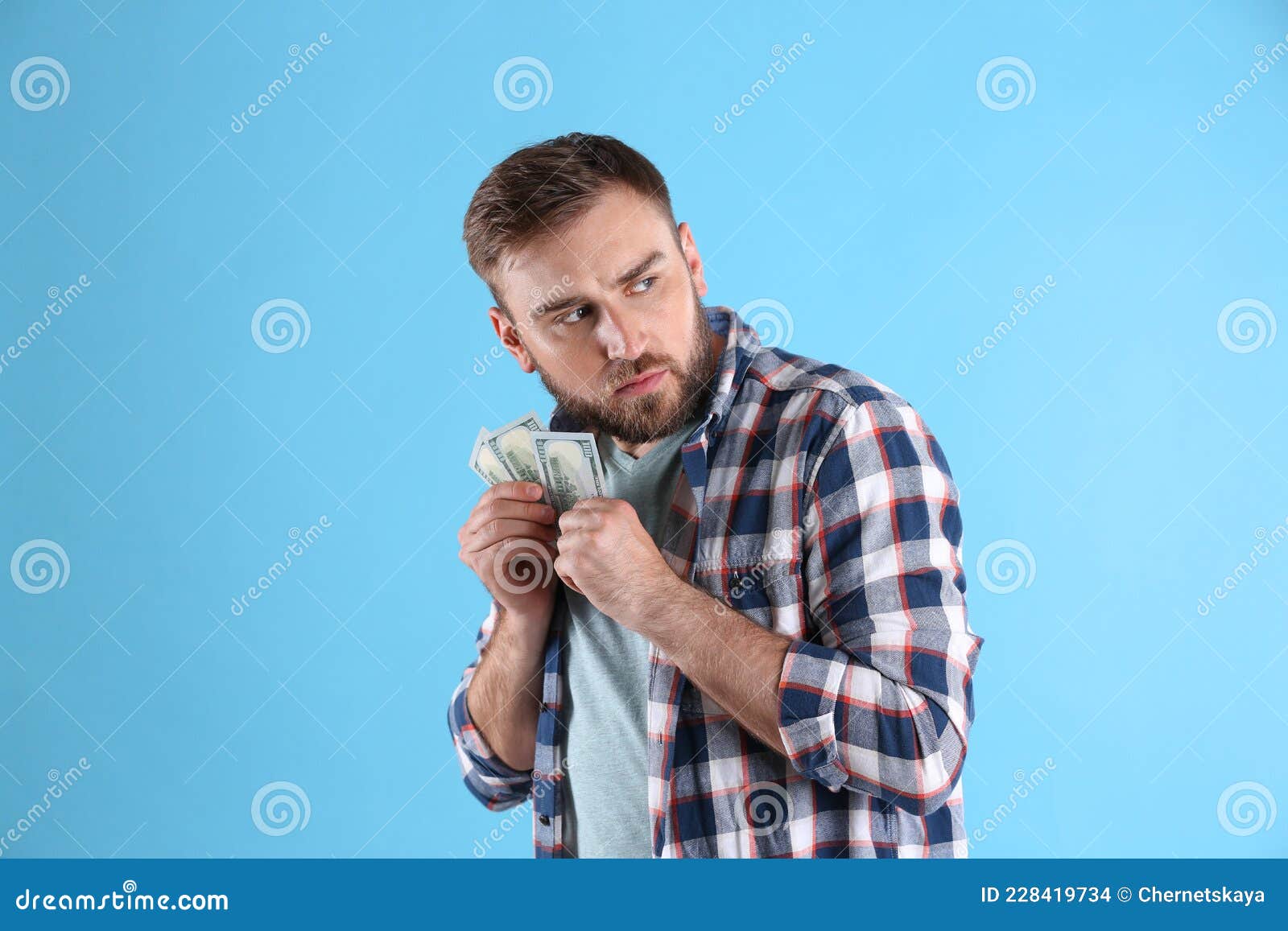 Greedy Young Man Hiding Money on Light Blue Background Stock Photo