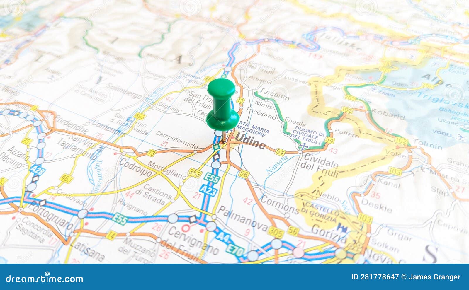 a green board pin stuck in udine on a map of italy