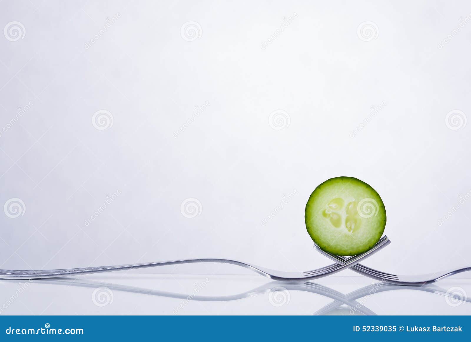 Green cucumber composition. Green cucumber slice on two intertwined forks on reflective top