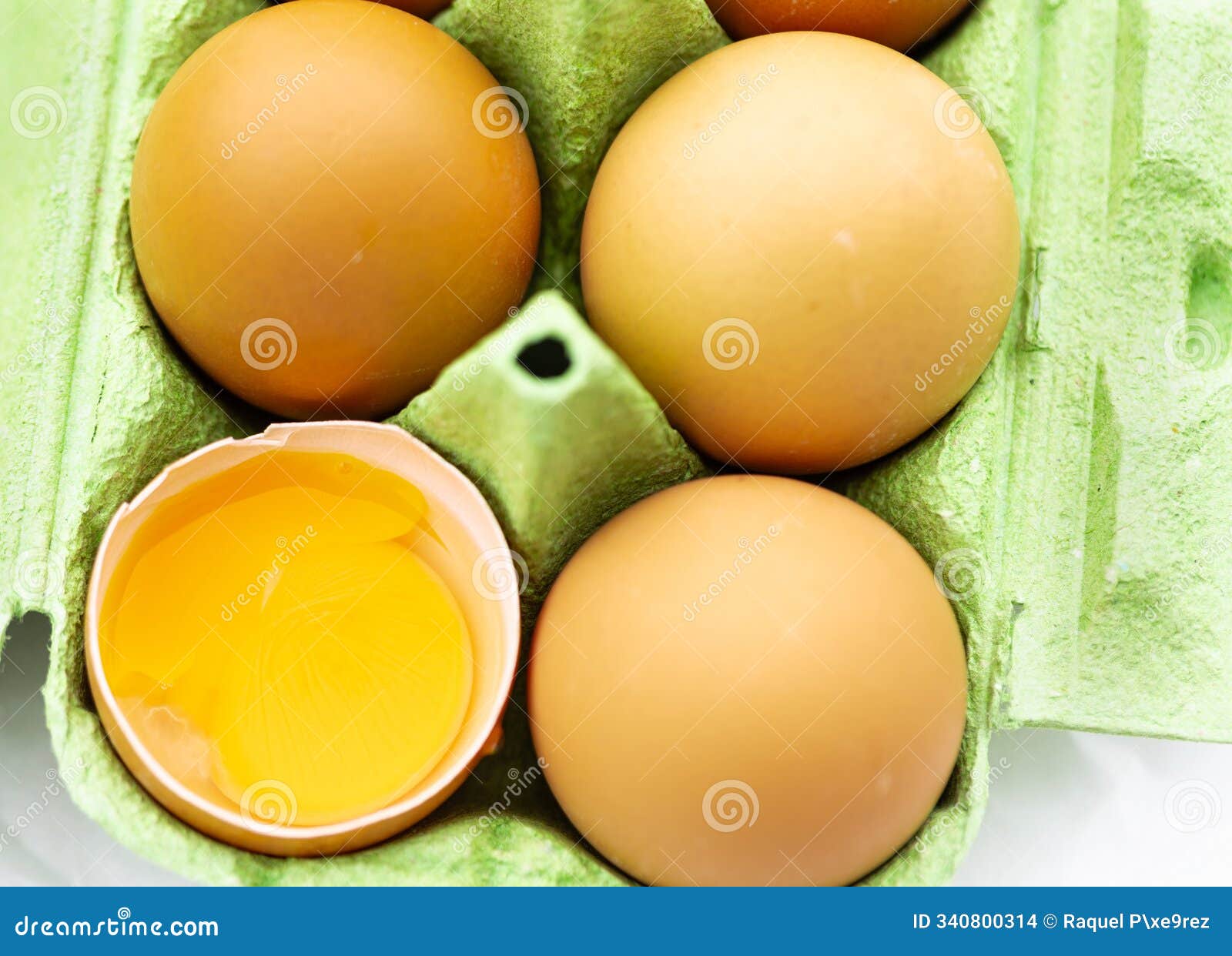 green egg carton with three whole eggs and one broken egg yolk