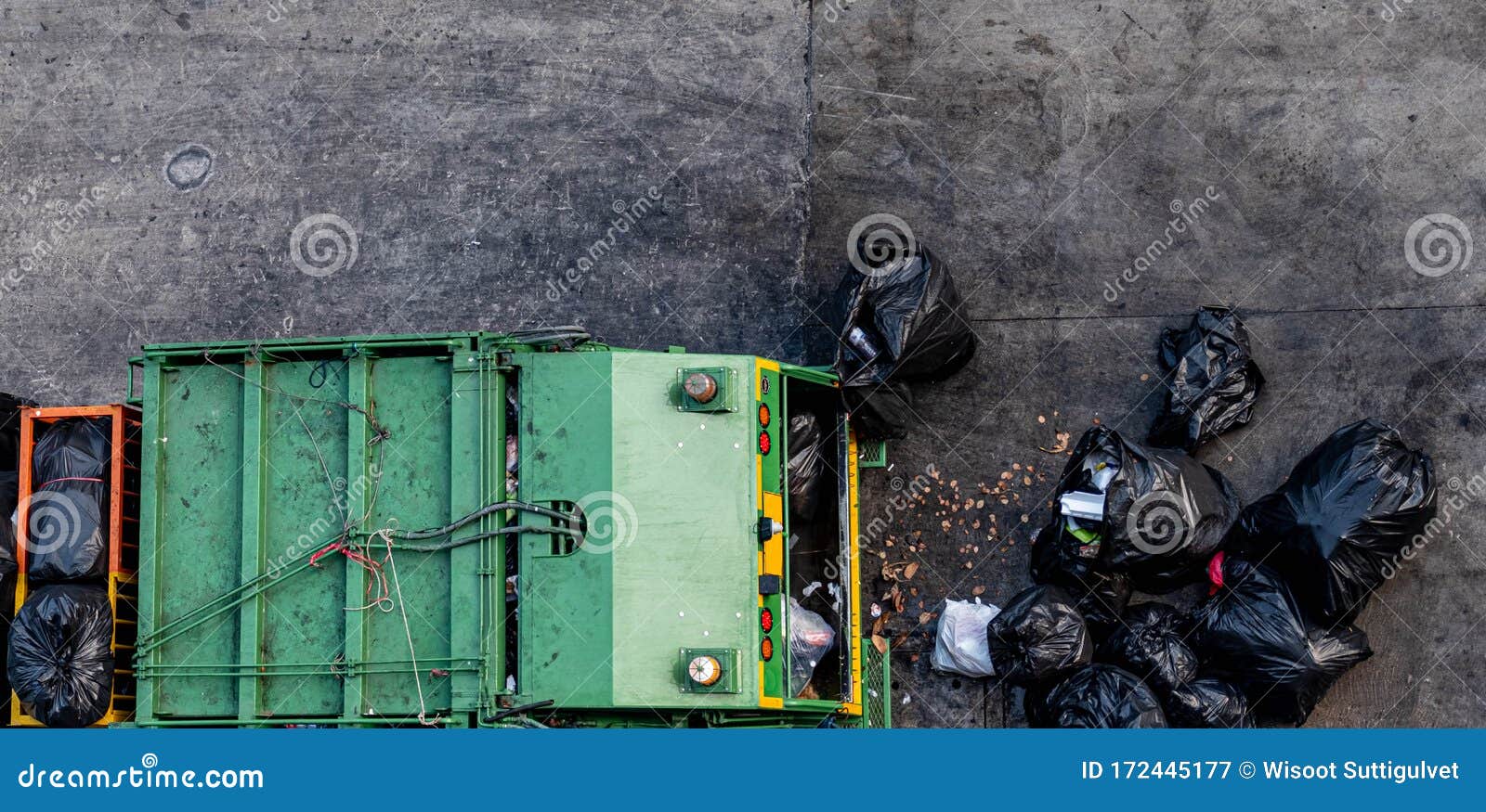 green garbage truck collecting a large number of black garbage bags that are tied up on the sidewalk to discard viewed from the to