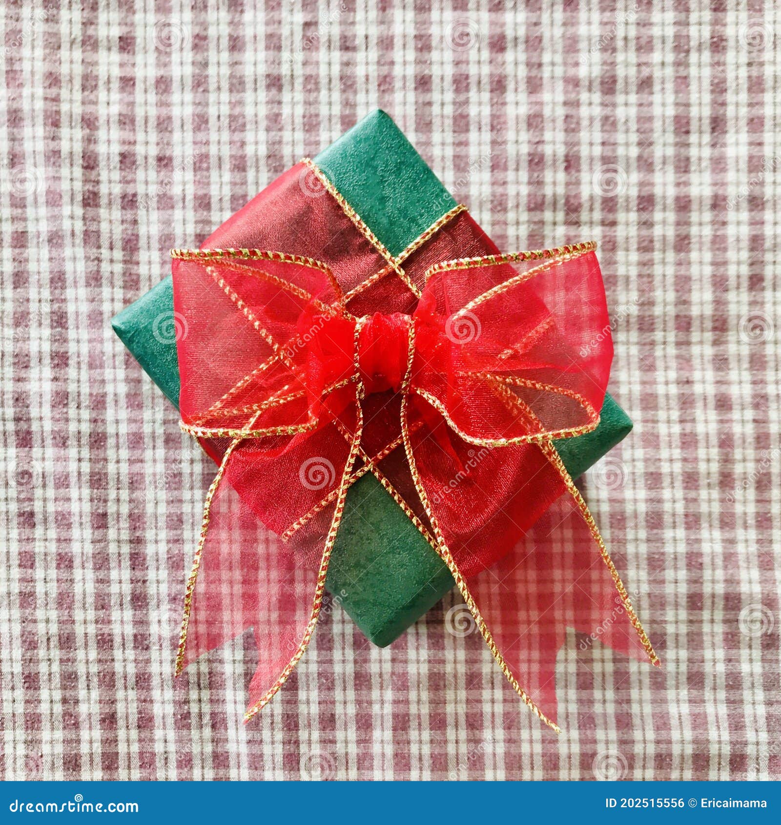 green gift with red ribbon on red white plaid tablecloth background.