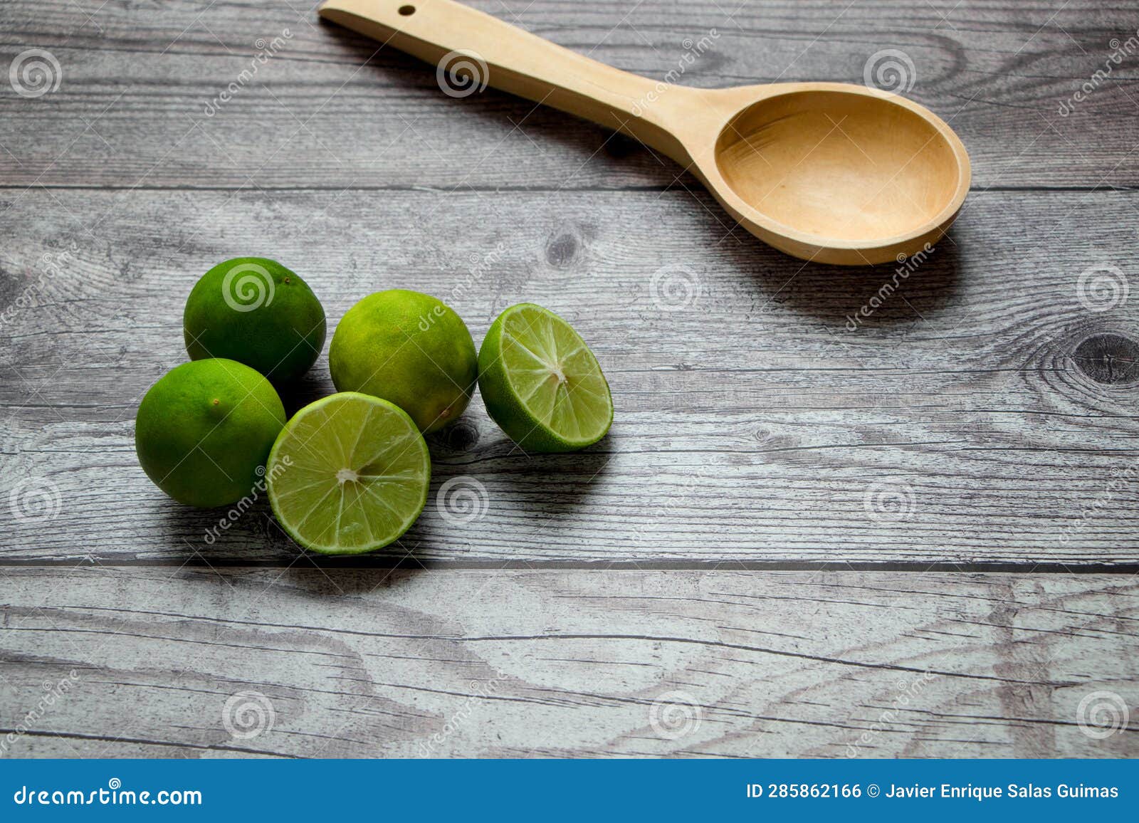 green lemons and wooden spoon on a rustic table