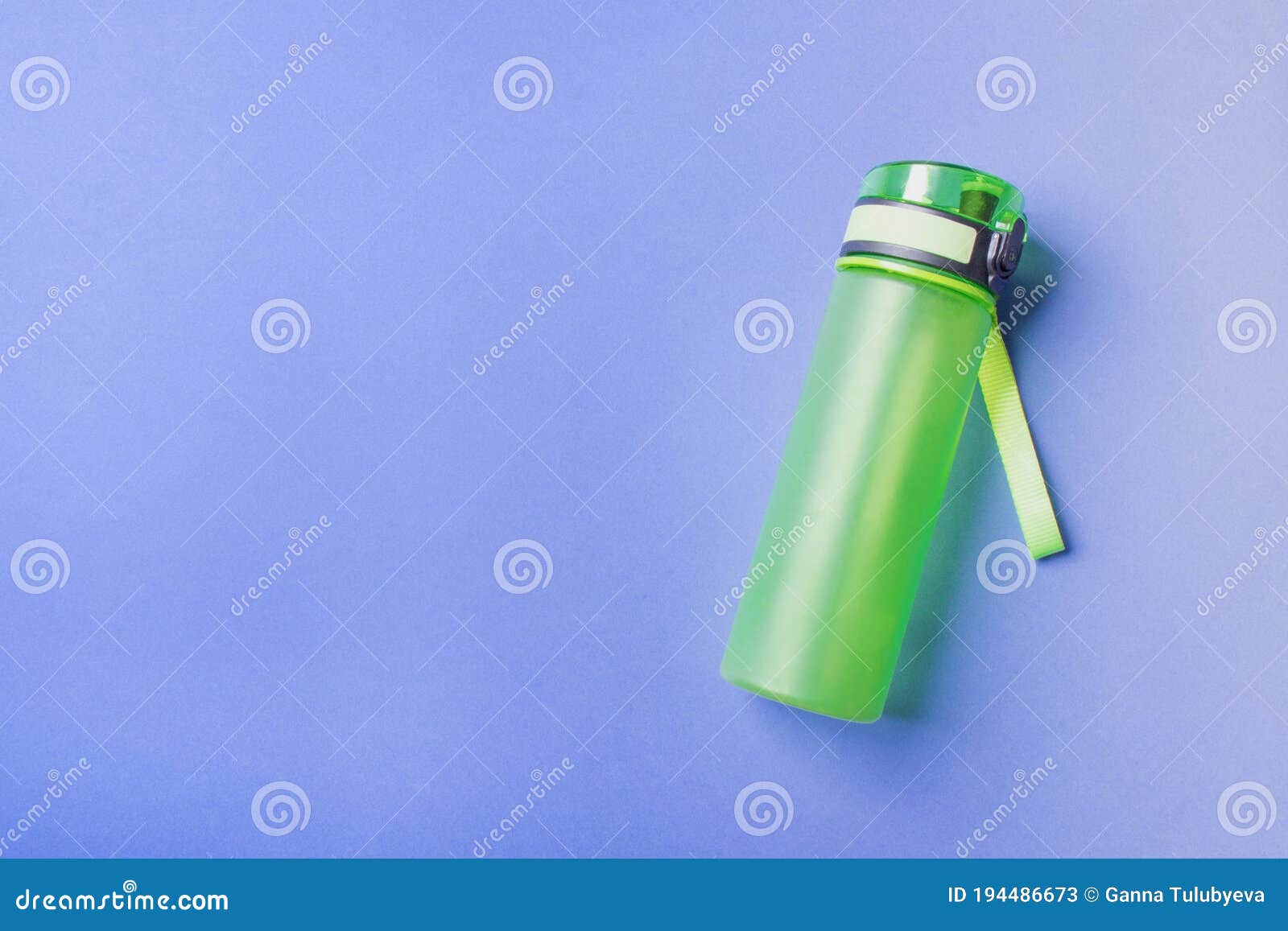 Green Plastic Sport Bottle Lying on Right Side of Blue Background with