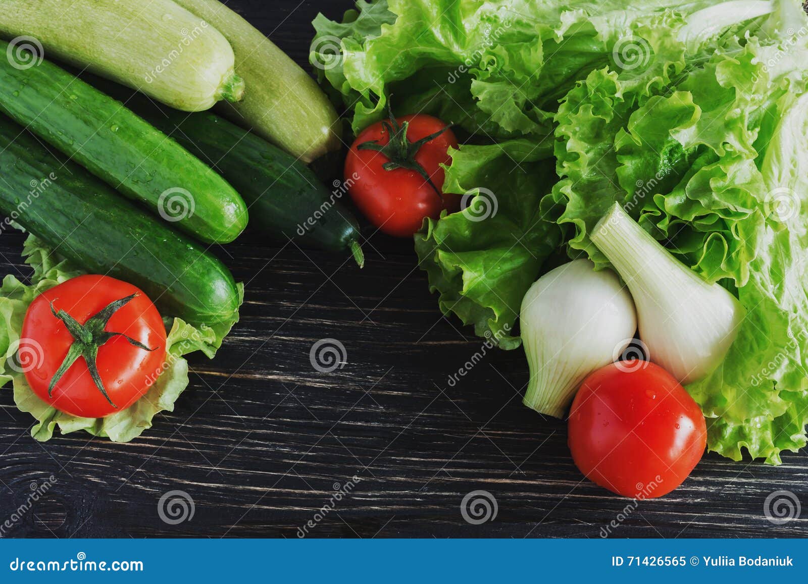 Green salad, tomatoes, cucumbers, zucchini, squash, and onion on black rustic wooden background . Group of fresh vegetables