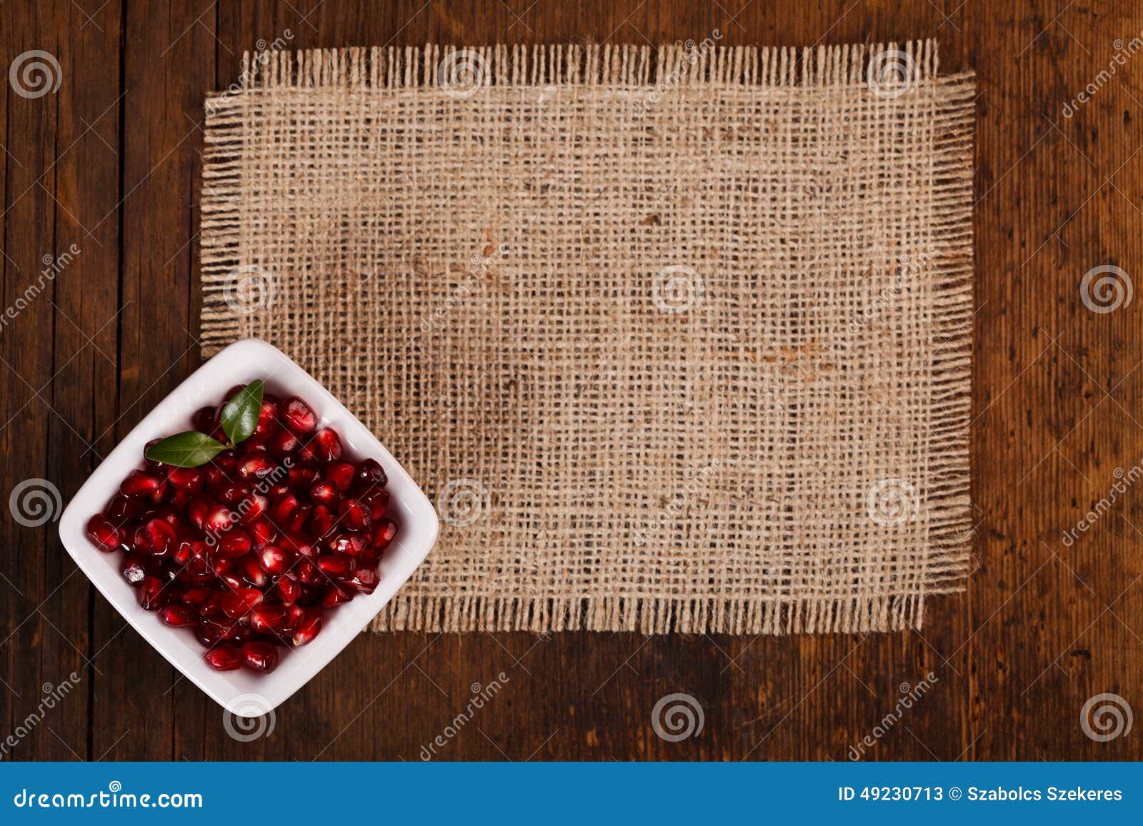 Grenadine seeds in white plate on canvas, wooden background, upper view