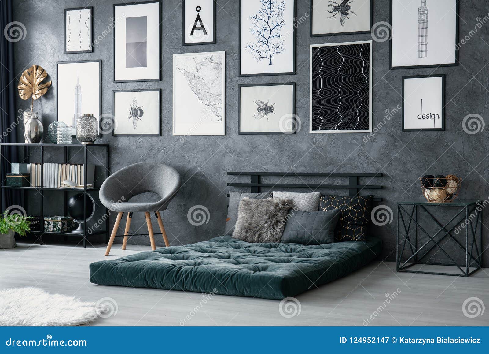 grey armchair next to green mattress in bedroom interior with gallery of posters. real photo