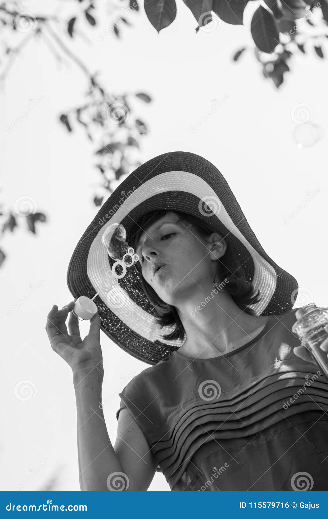 greyscale portrait of an attractive woman in a wide brimmed sunhat blowing bubbles