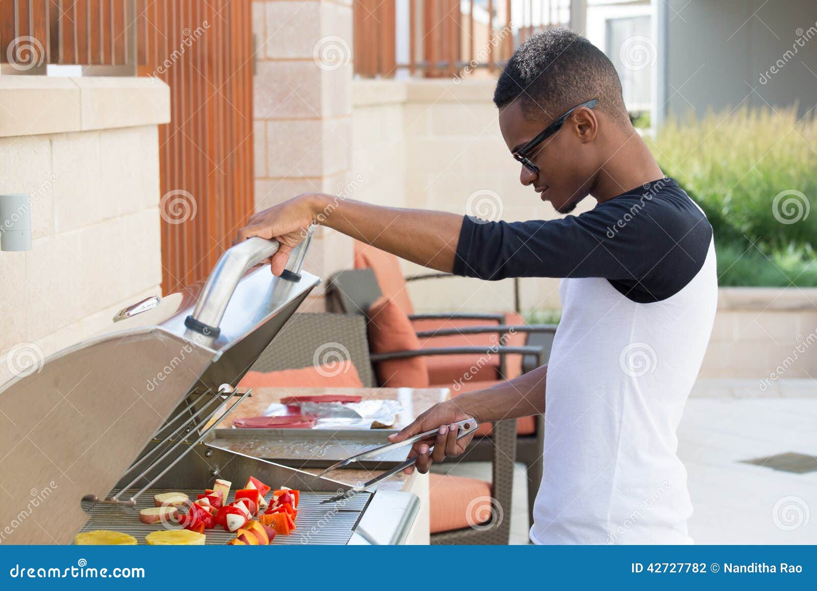 Grilling. Retrato del primer, individuo joven hermoso con los vidrios grandes que asa a la parilla la comida deliciosa, fondo exterior aislado